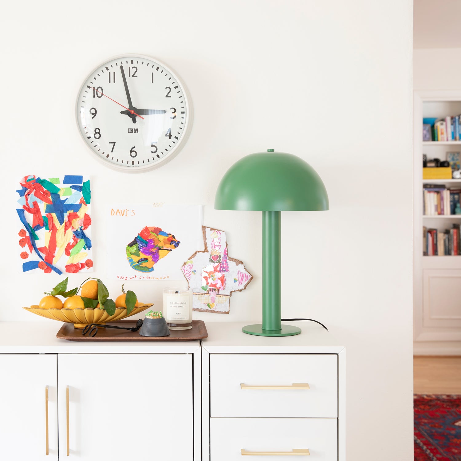 clock on a wall and a green table lamp on a cabinet