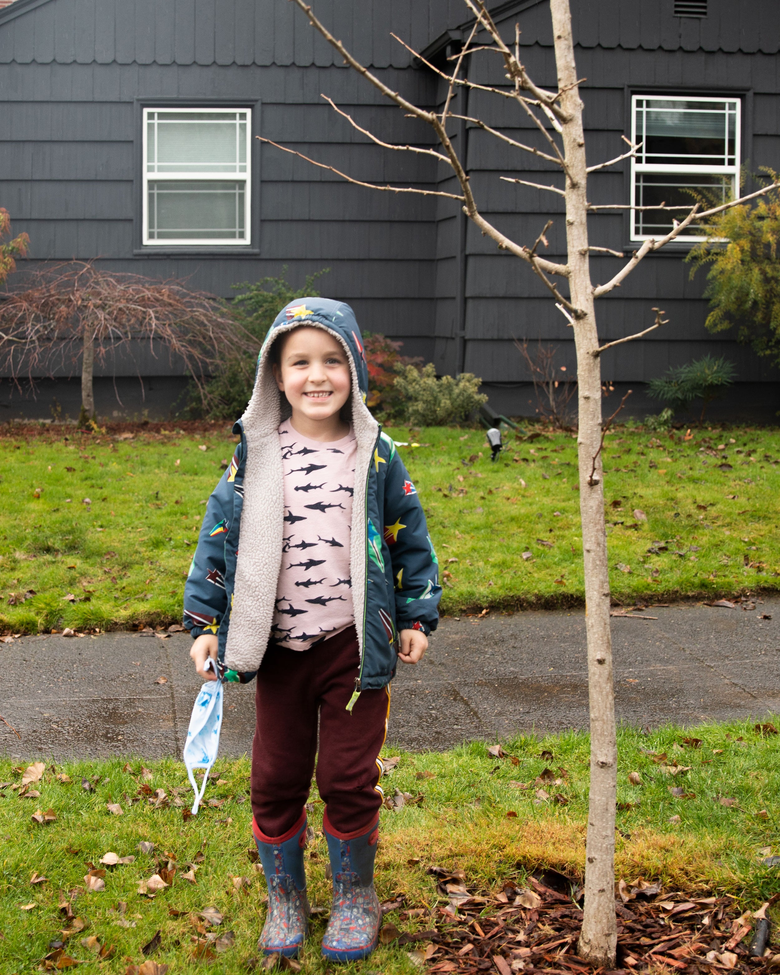 child standing in front of a tree and a house