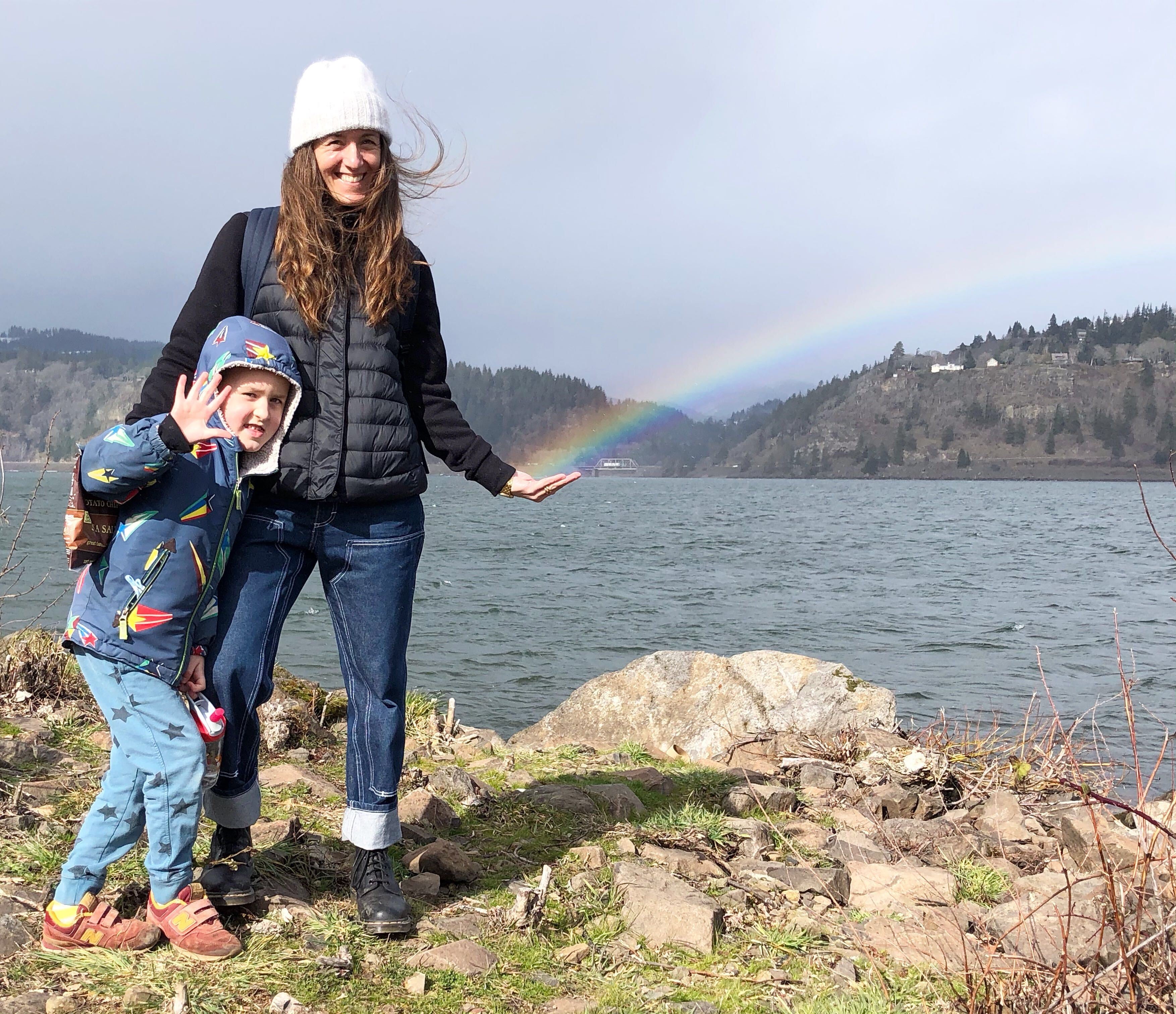 person and two children posing for a picture by a body of water and a rainbow