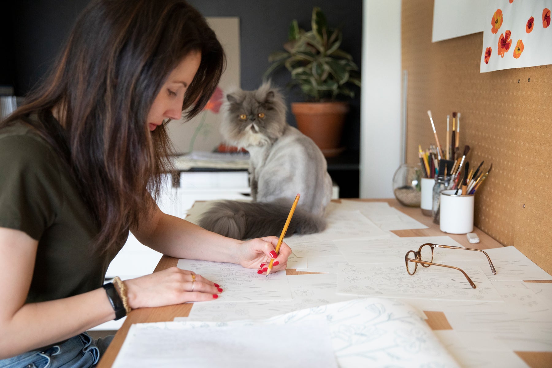 woman drawing at her desk with a gray cat on the desk