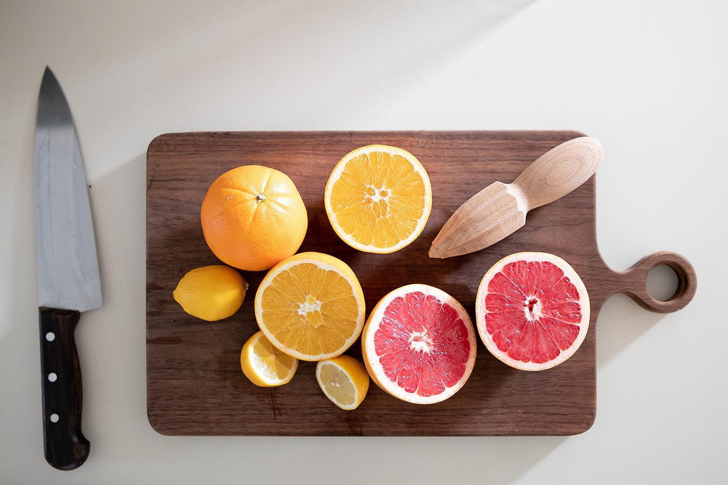 cut citrus and a juicer tool on a cutting board next to a knife