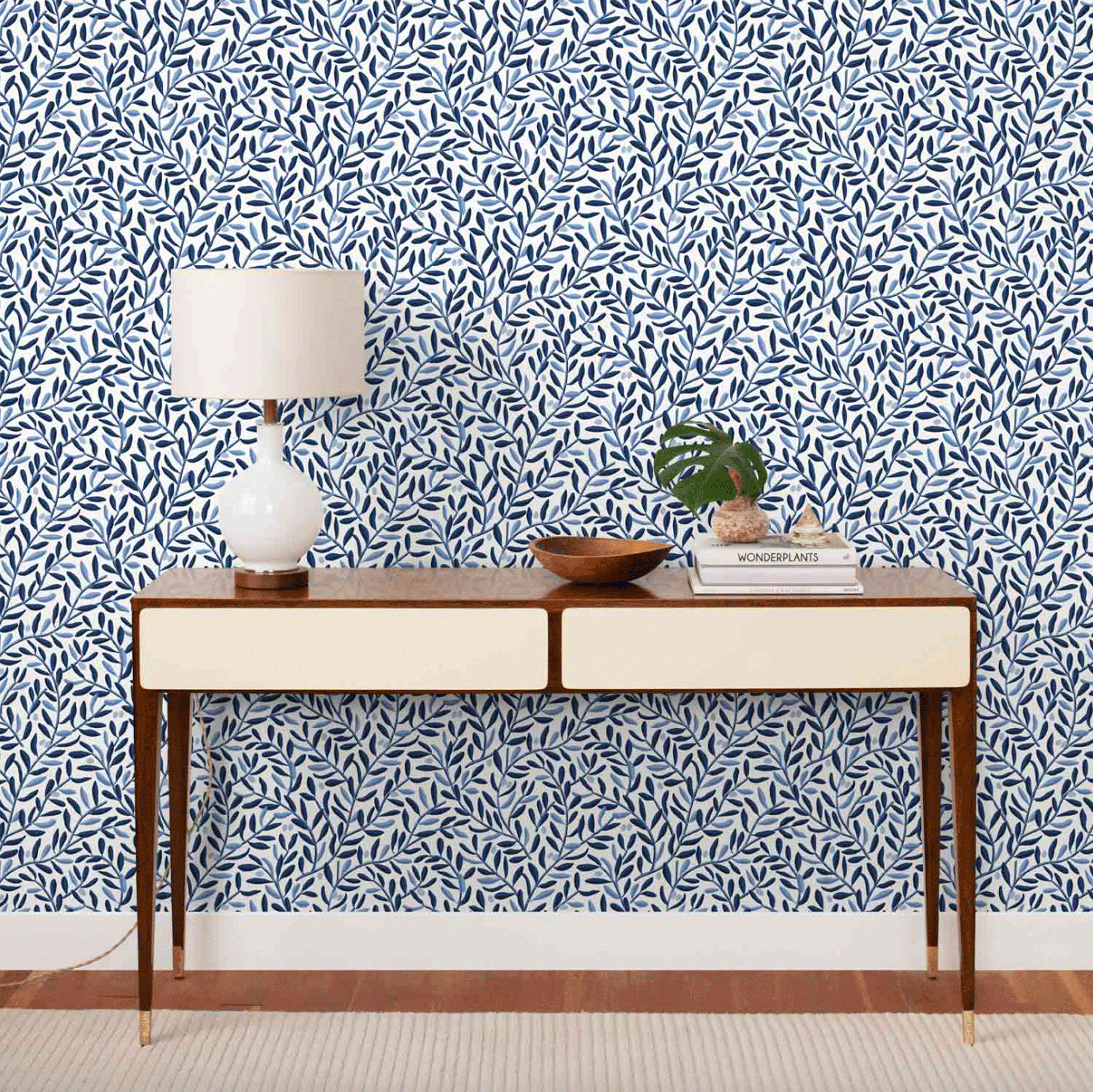 Blue and white wallpaper is on the wall behind an entryway table