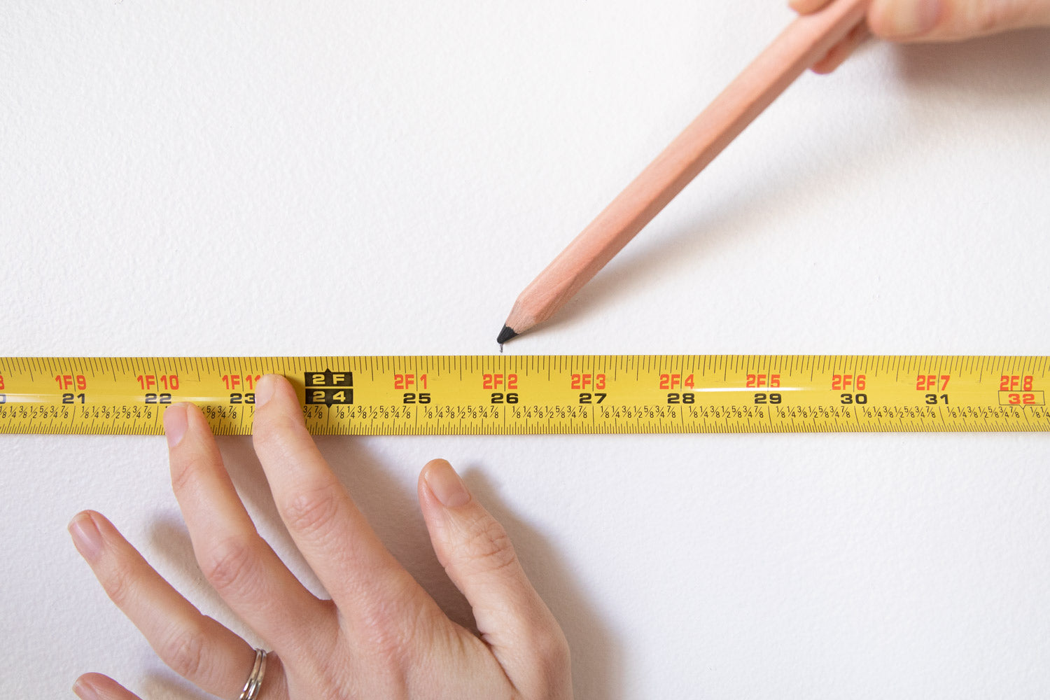 person marking a measurement using a pencil and measuring tape