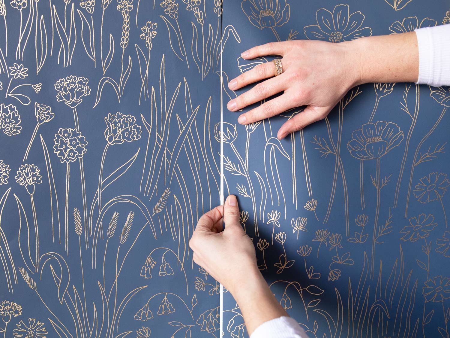 person attaching blue patterned wallpaper