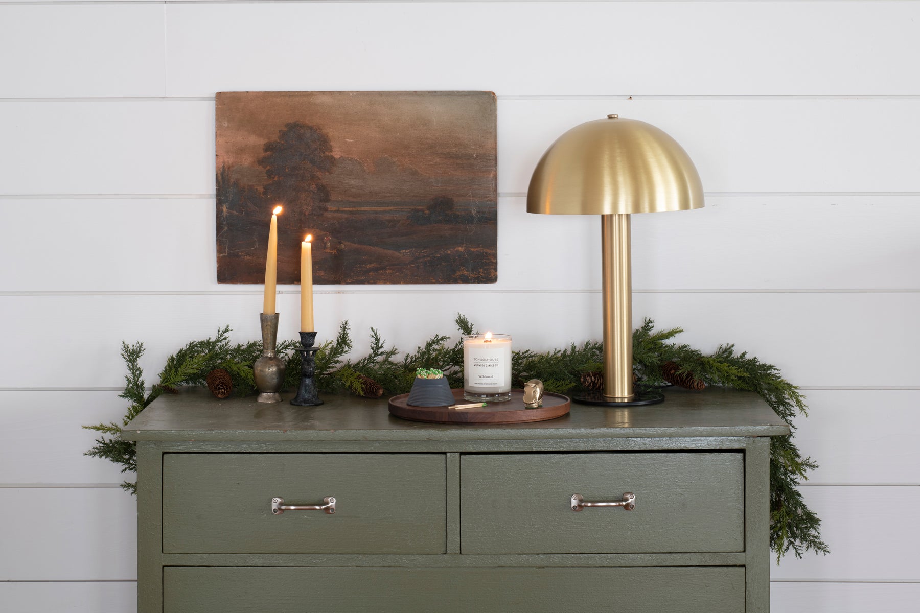 green dresser with a gold table lamp and candles and greenery