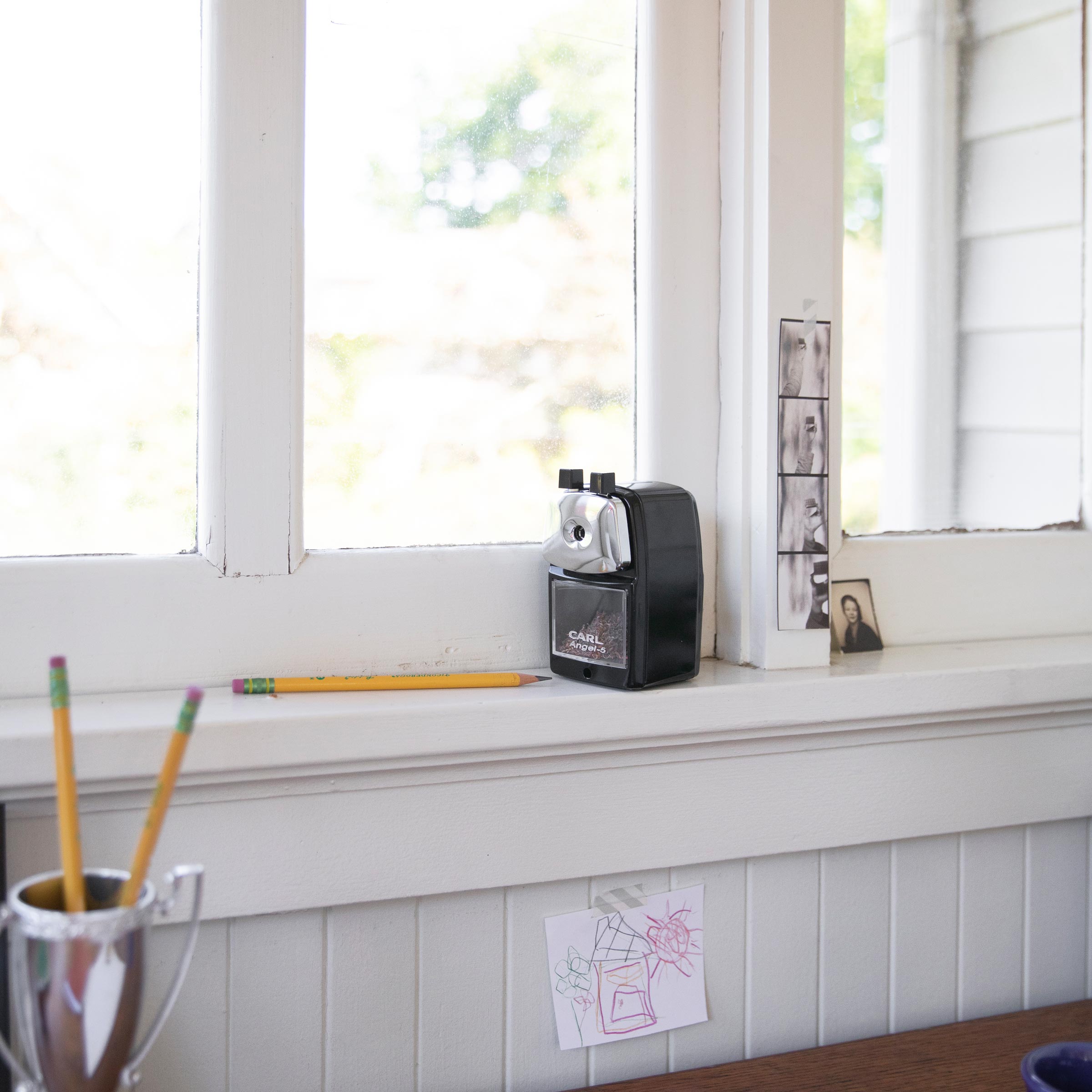 A black desktop pencil sharpener by the window with a pencil next to it.