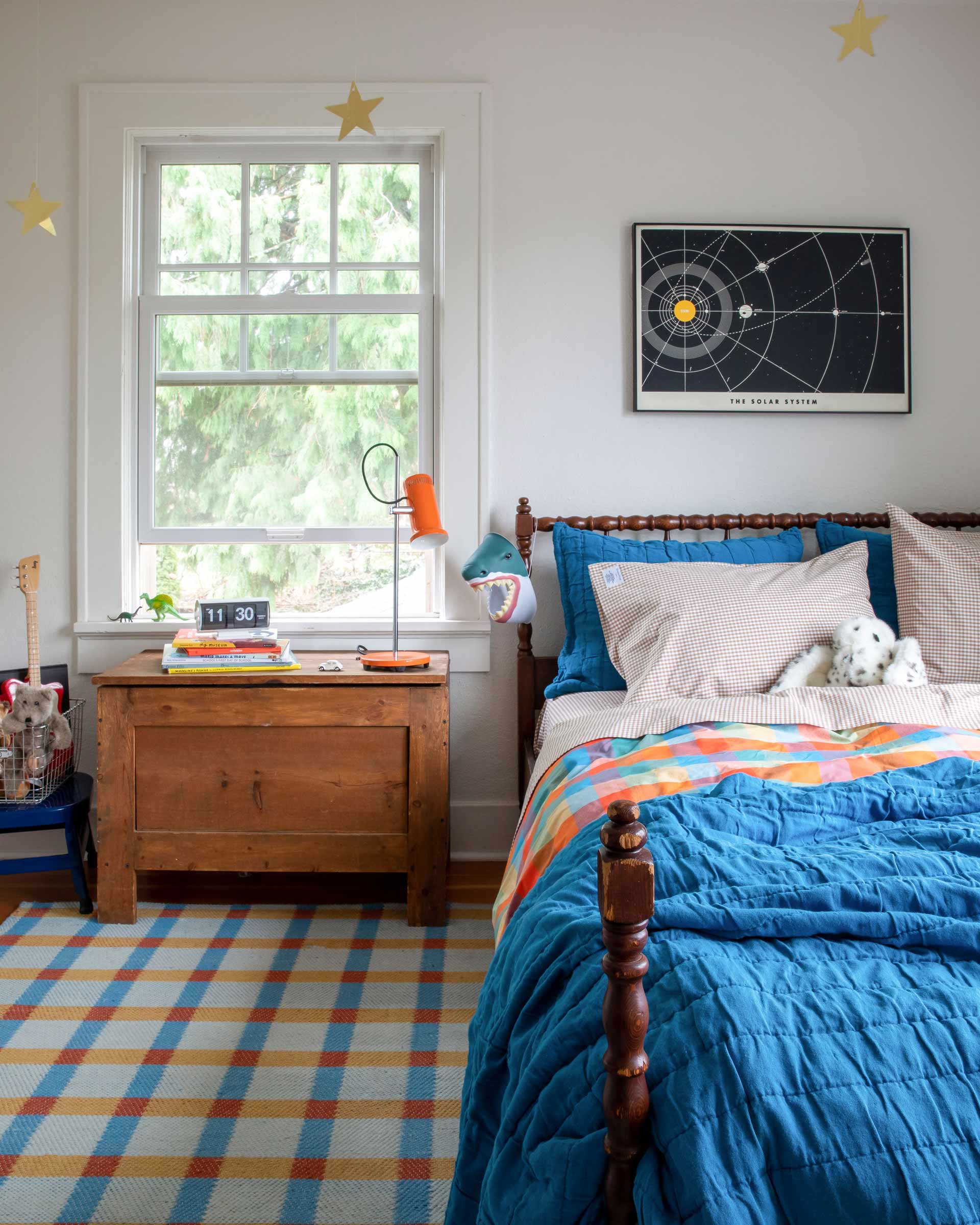 A colorful kid's bedroom with a blue quilt and a plaid rug.