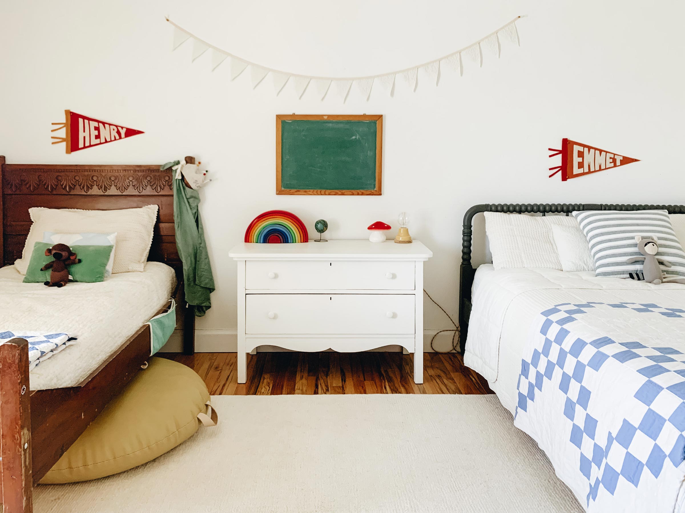 A kid's room with two beds, a chalkboard, and a little table lamp. 