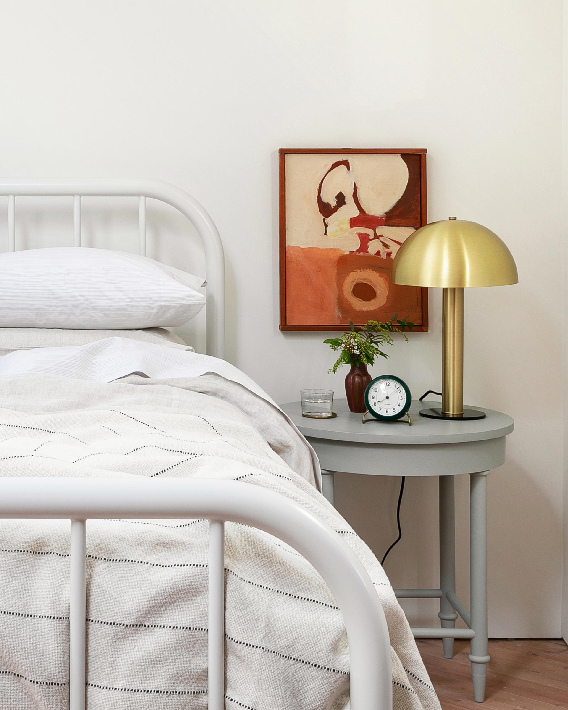 A brass Sidnie table lamp on a side table in a bedroom. 