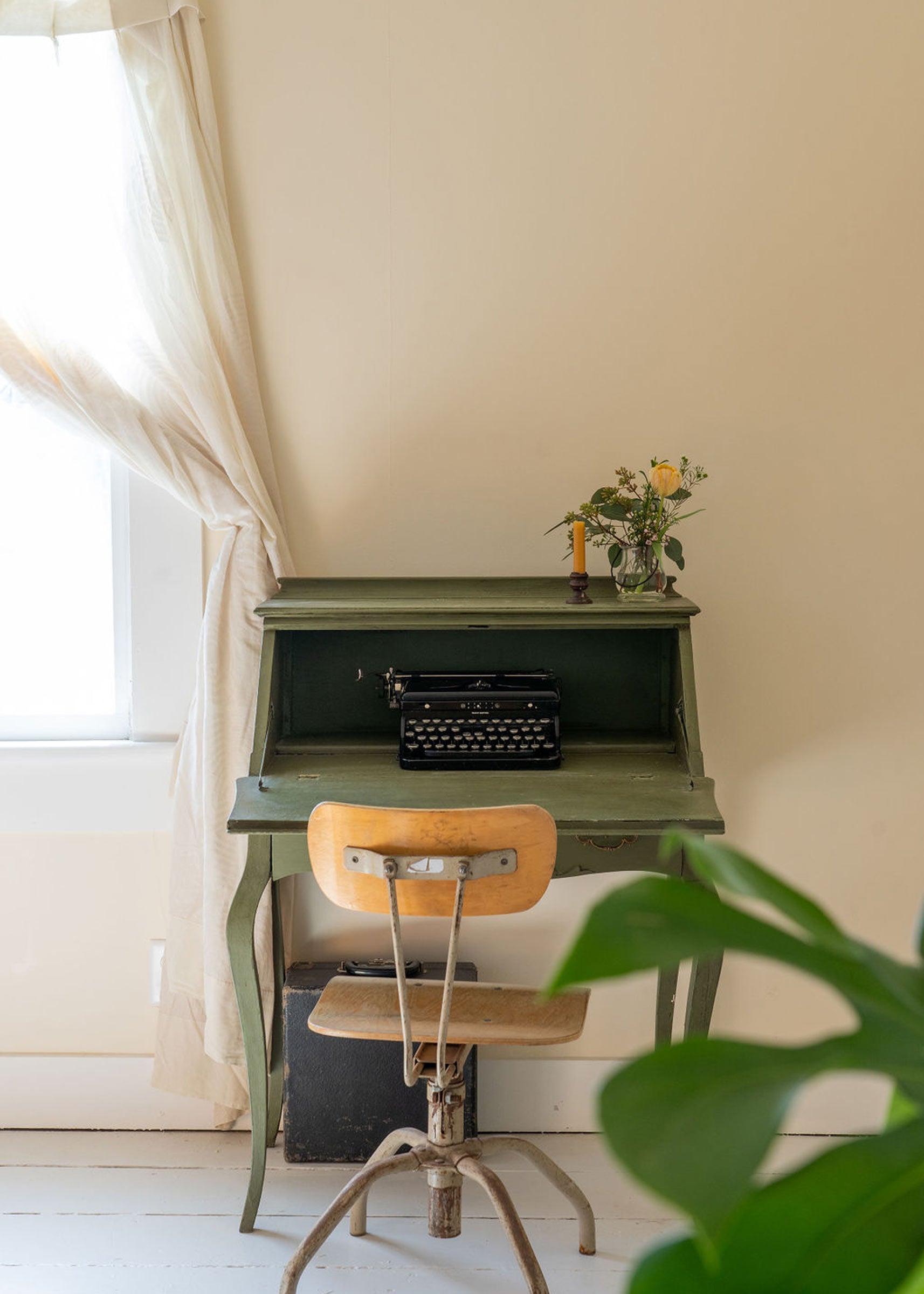 A typewriter in a bedroom with a drafting chair. 