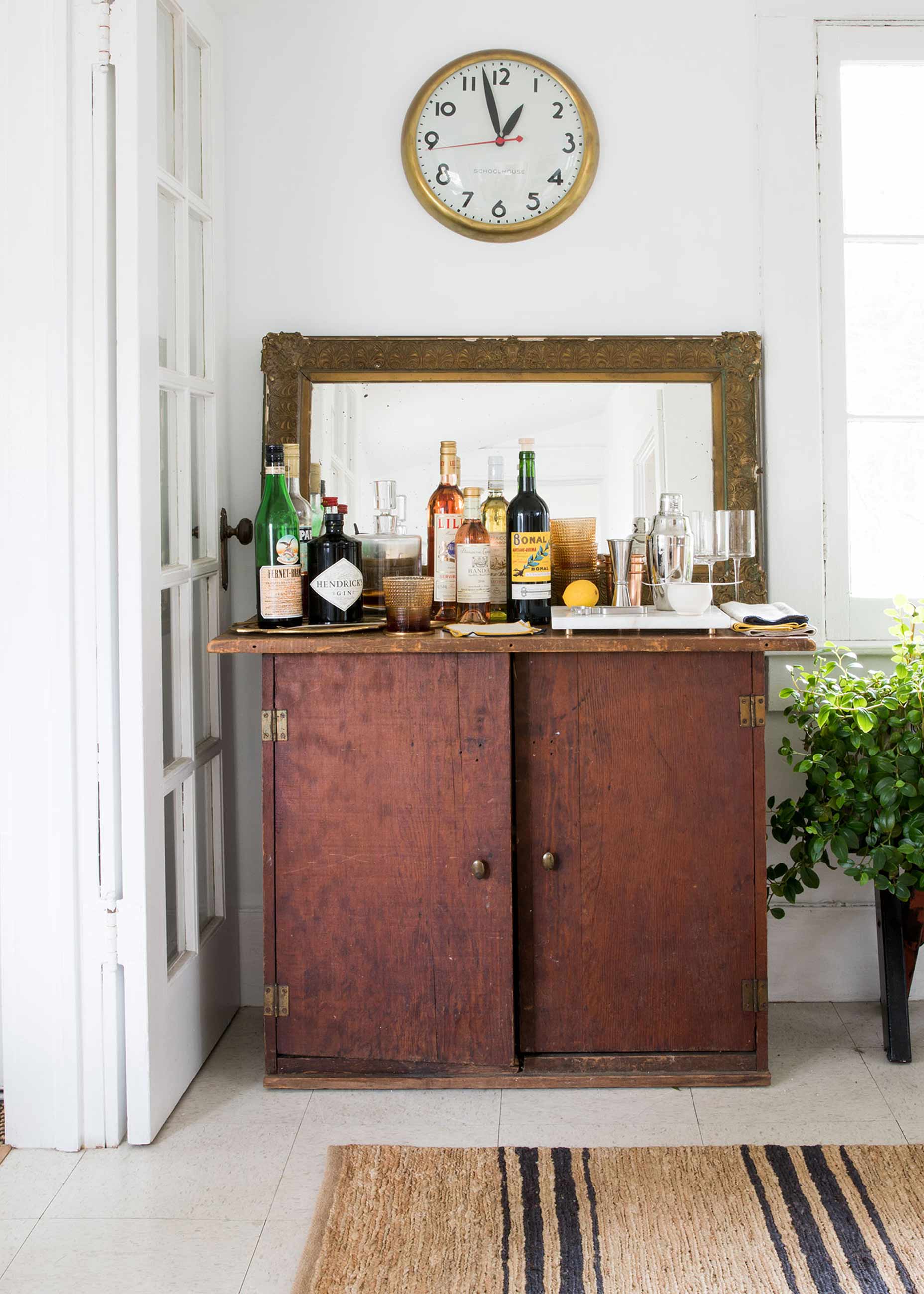 Antique bar cart with mirror behind it and clock above.