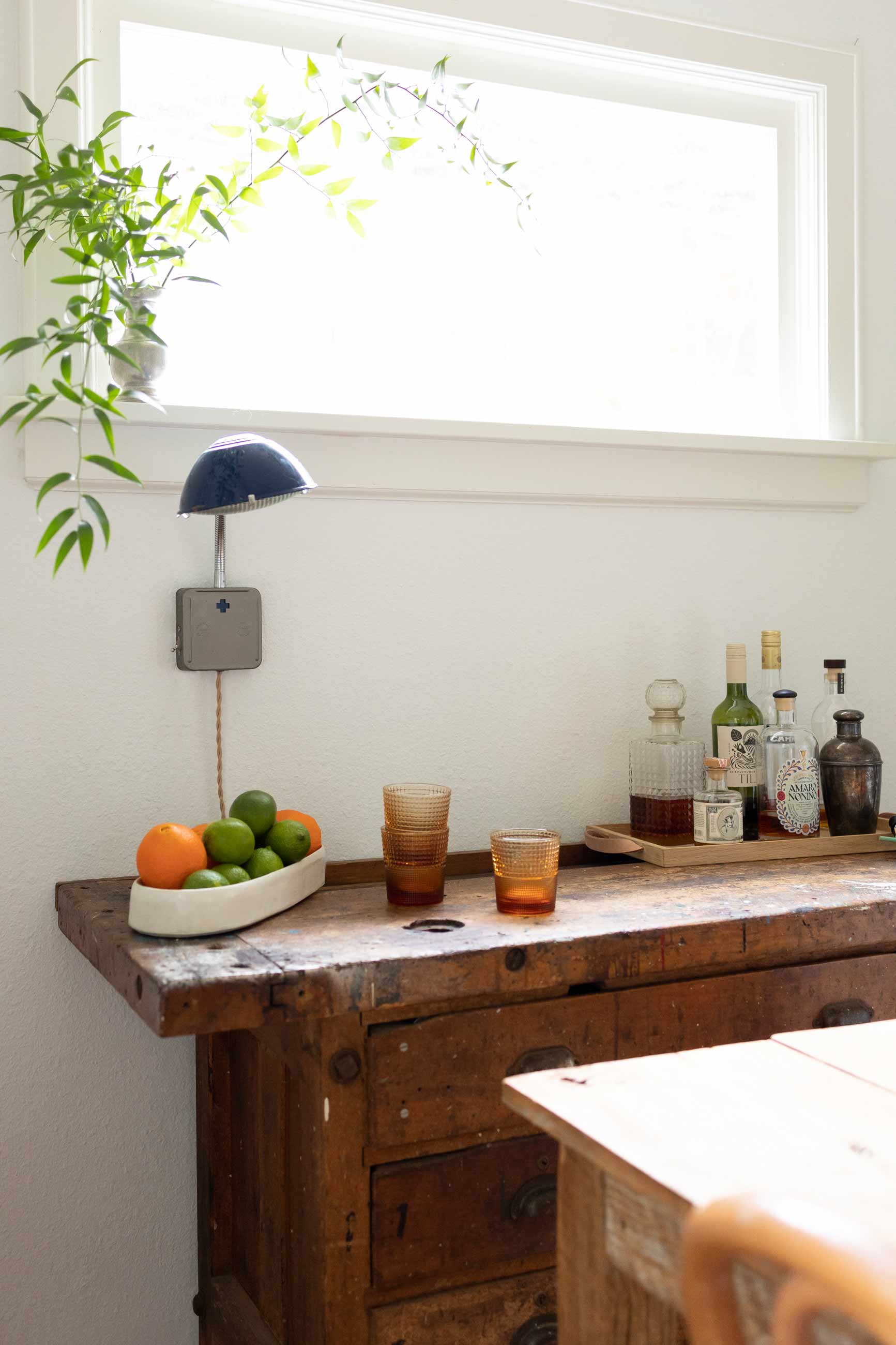 Vintage work bench converted into a modern bar cart with plug in wall sconce above.