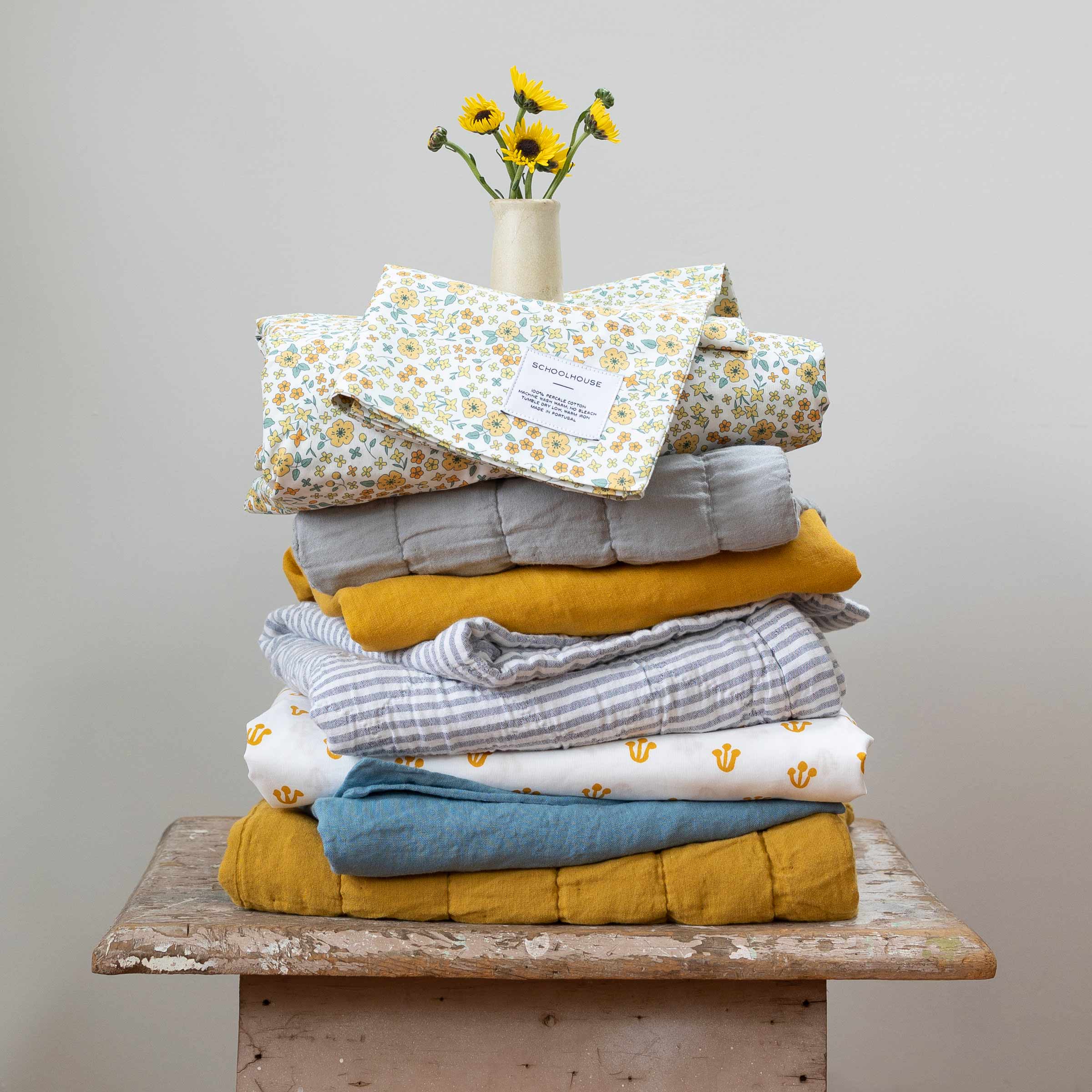 A bedding stack with floral vintage-inspired sheet sets and quilts. 