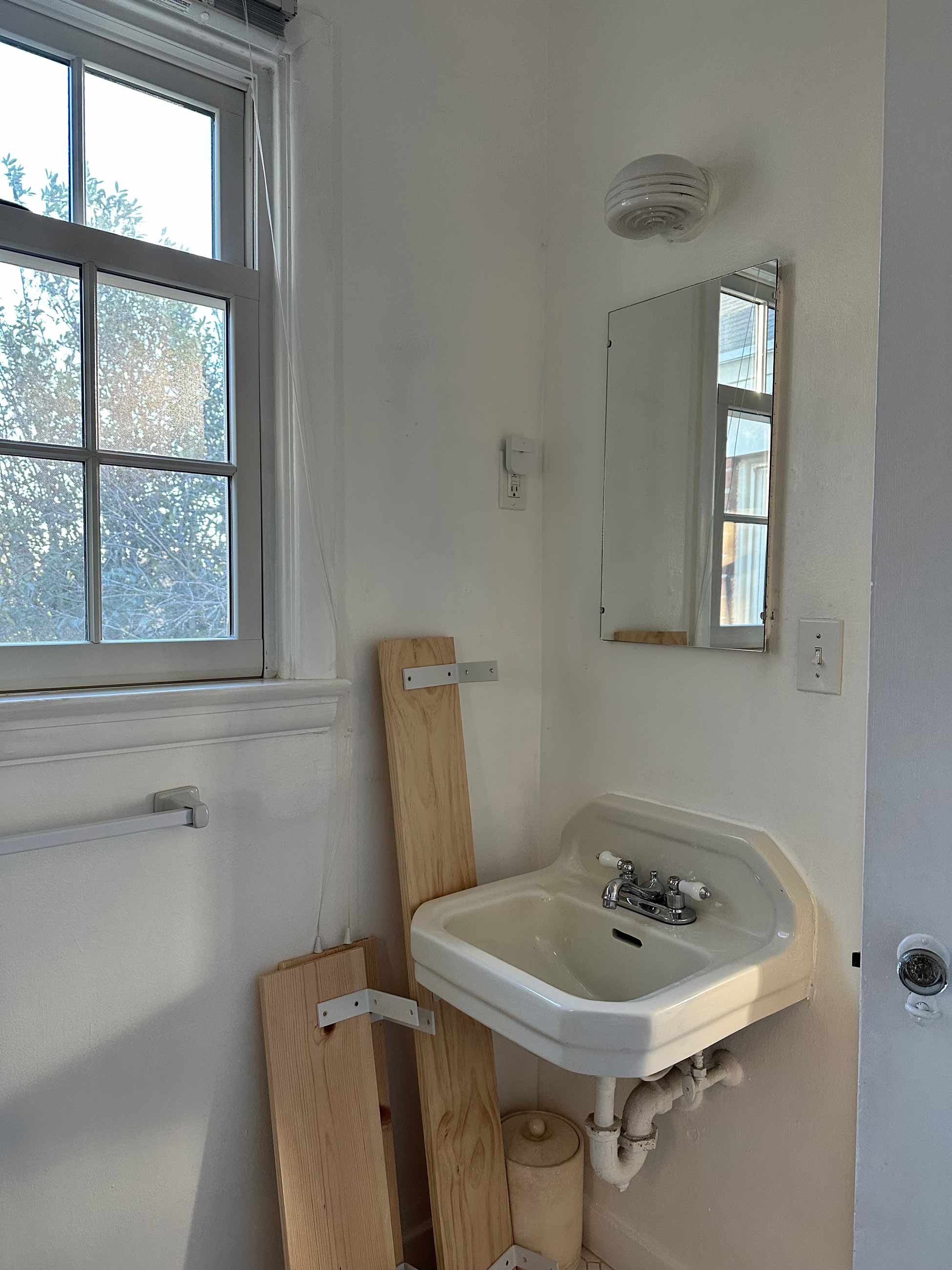 Before image of rental bathroom with white walls and outdated light fixture above sink.