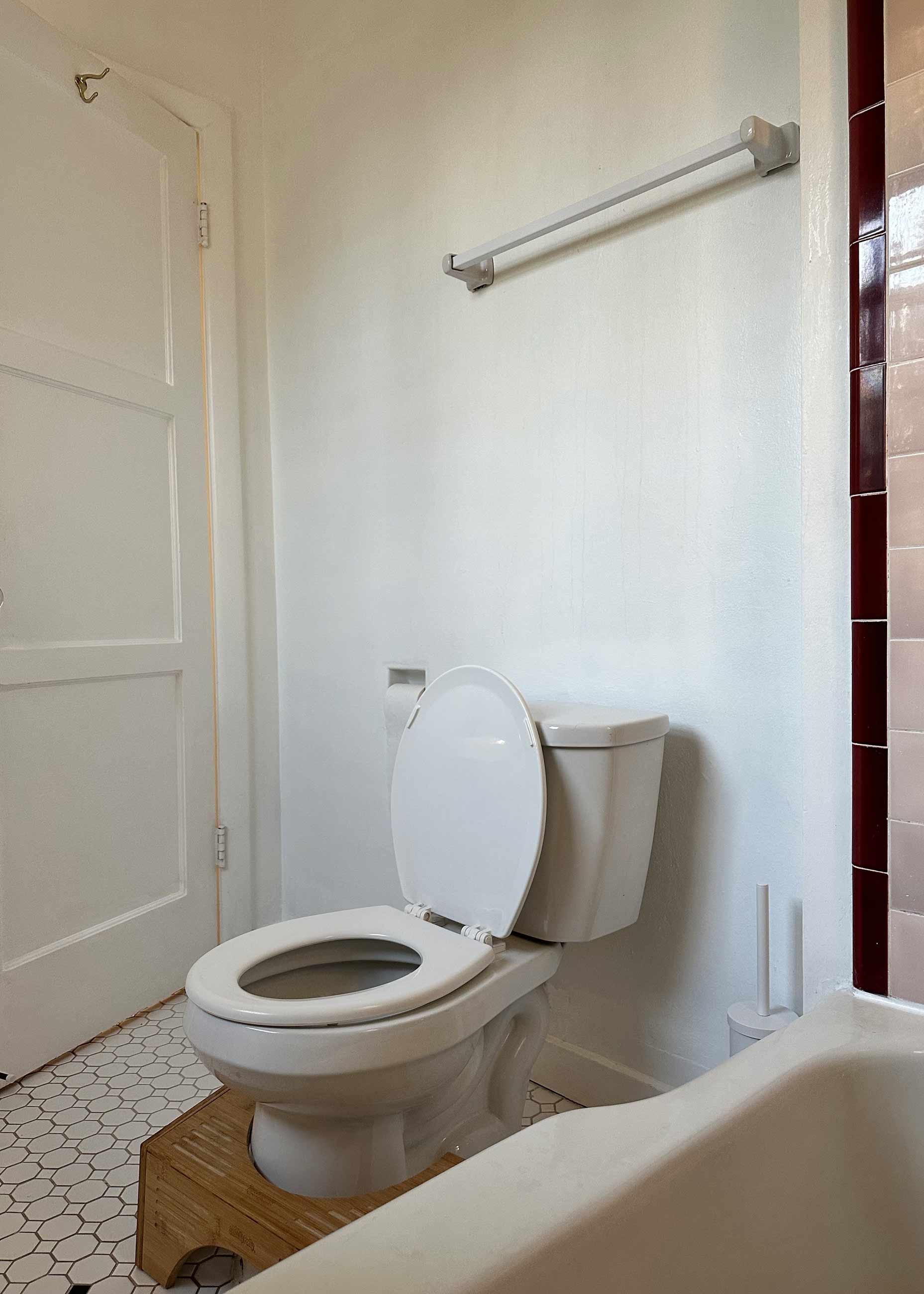 Before image of rental bathroom with plain white wall and outdated hardware.