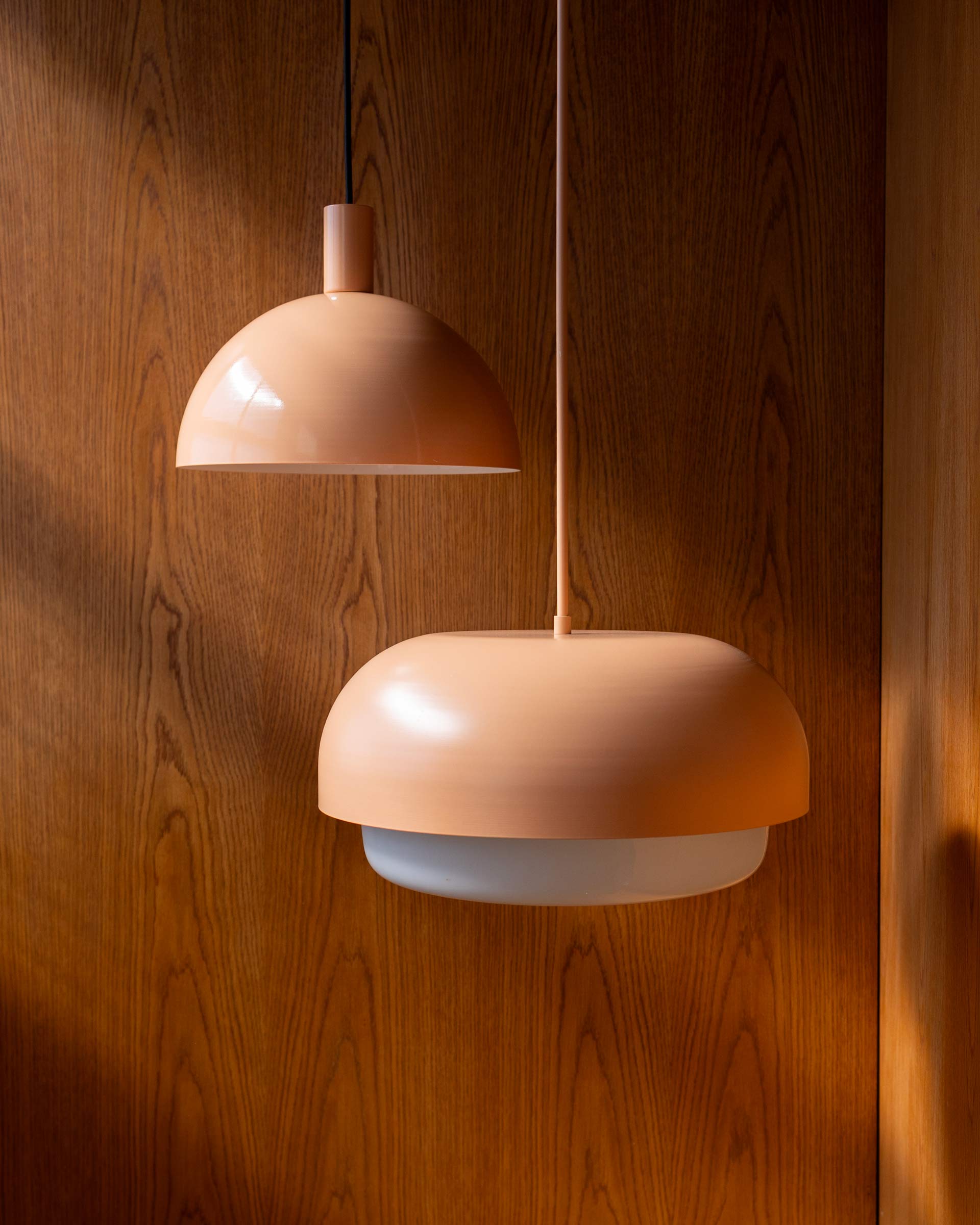 Two light pink pendants hanging on a wood backdrop.