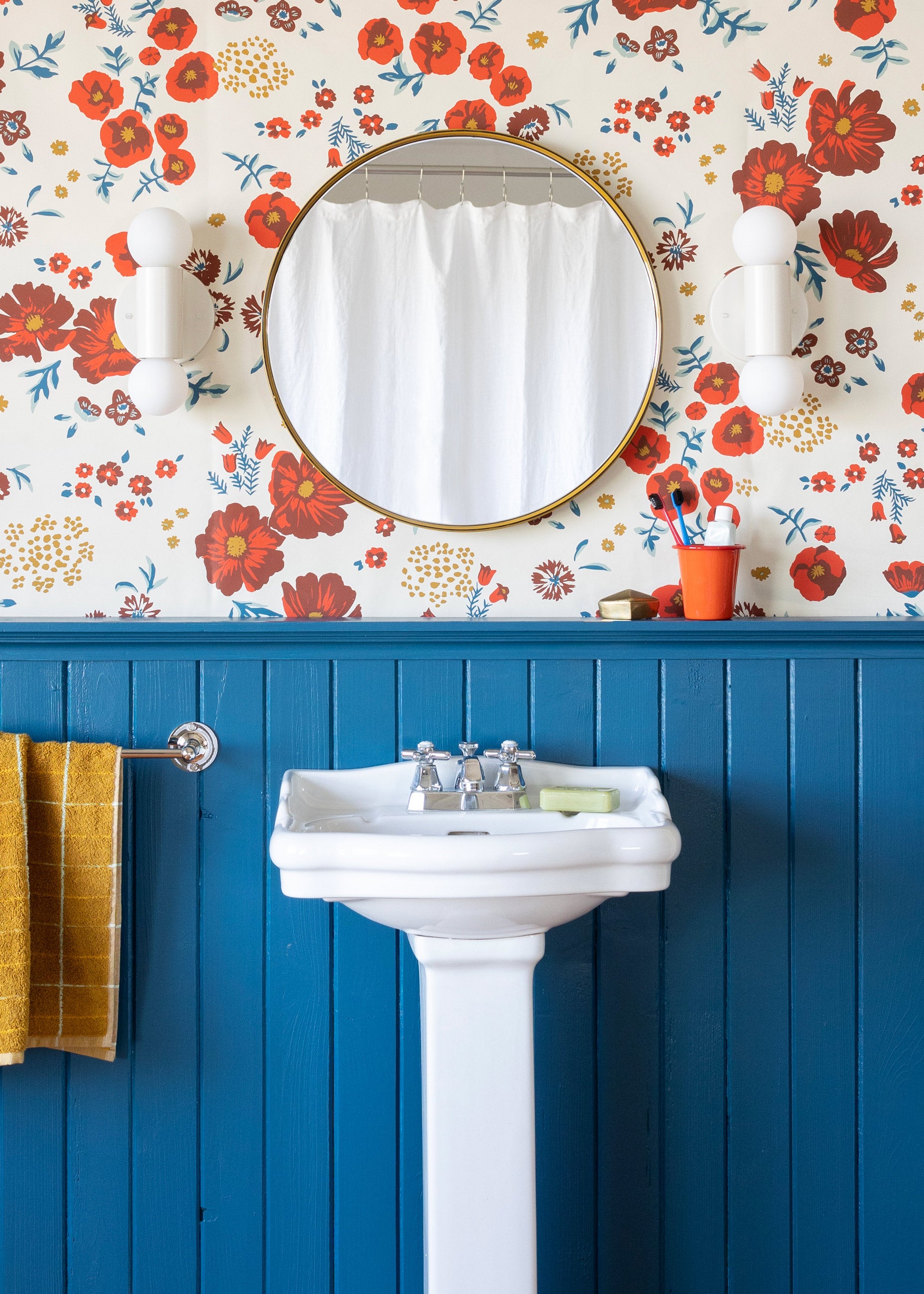 Blue wainscoting in bathroom with floral wallpaper above sink. 