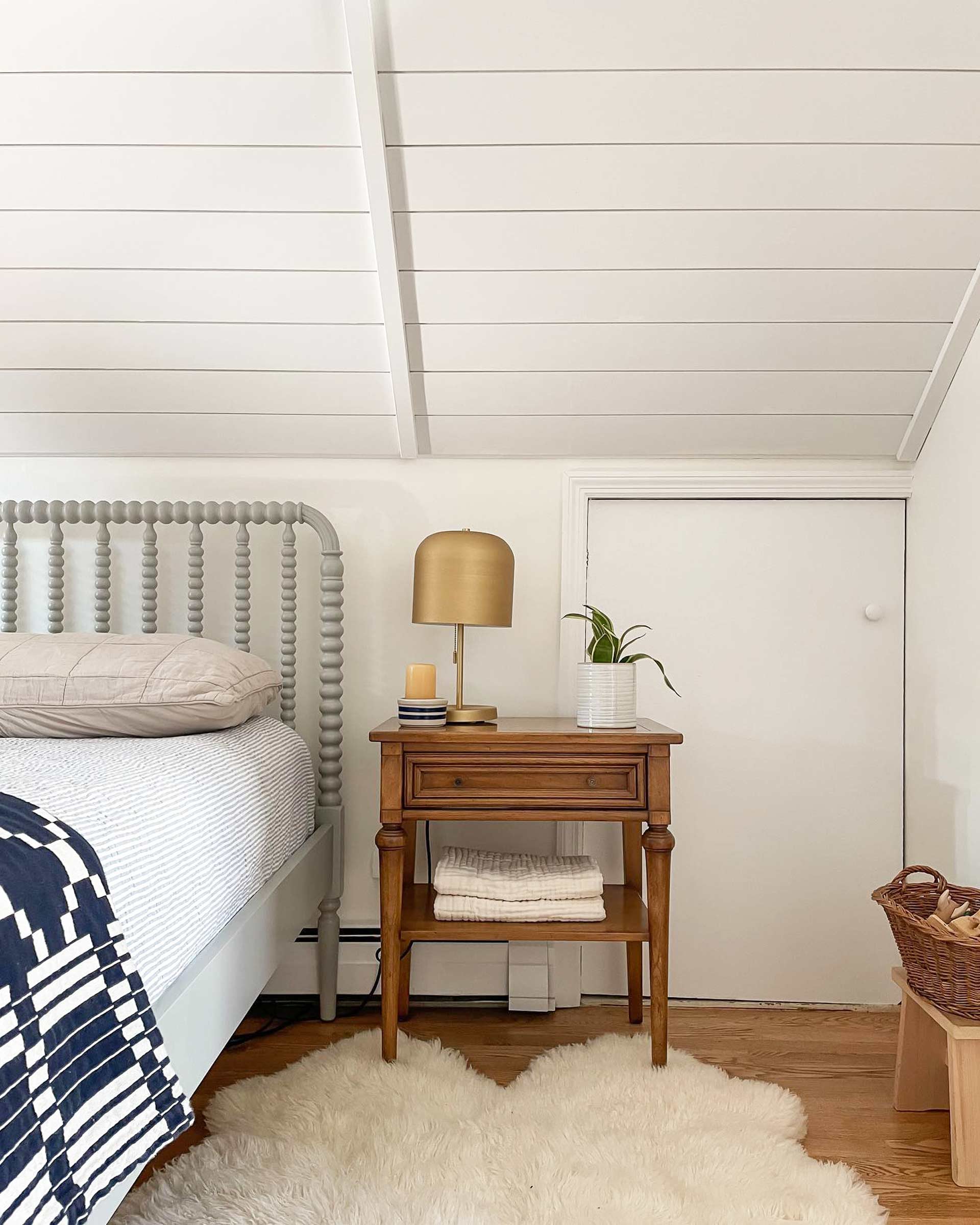 Cozy bedroom attic with a wooden side table and brass table lamp on top.