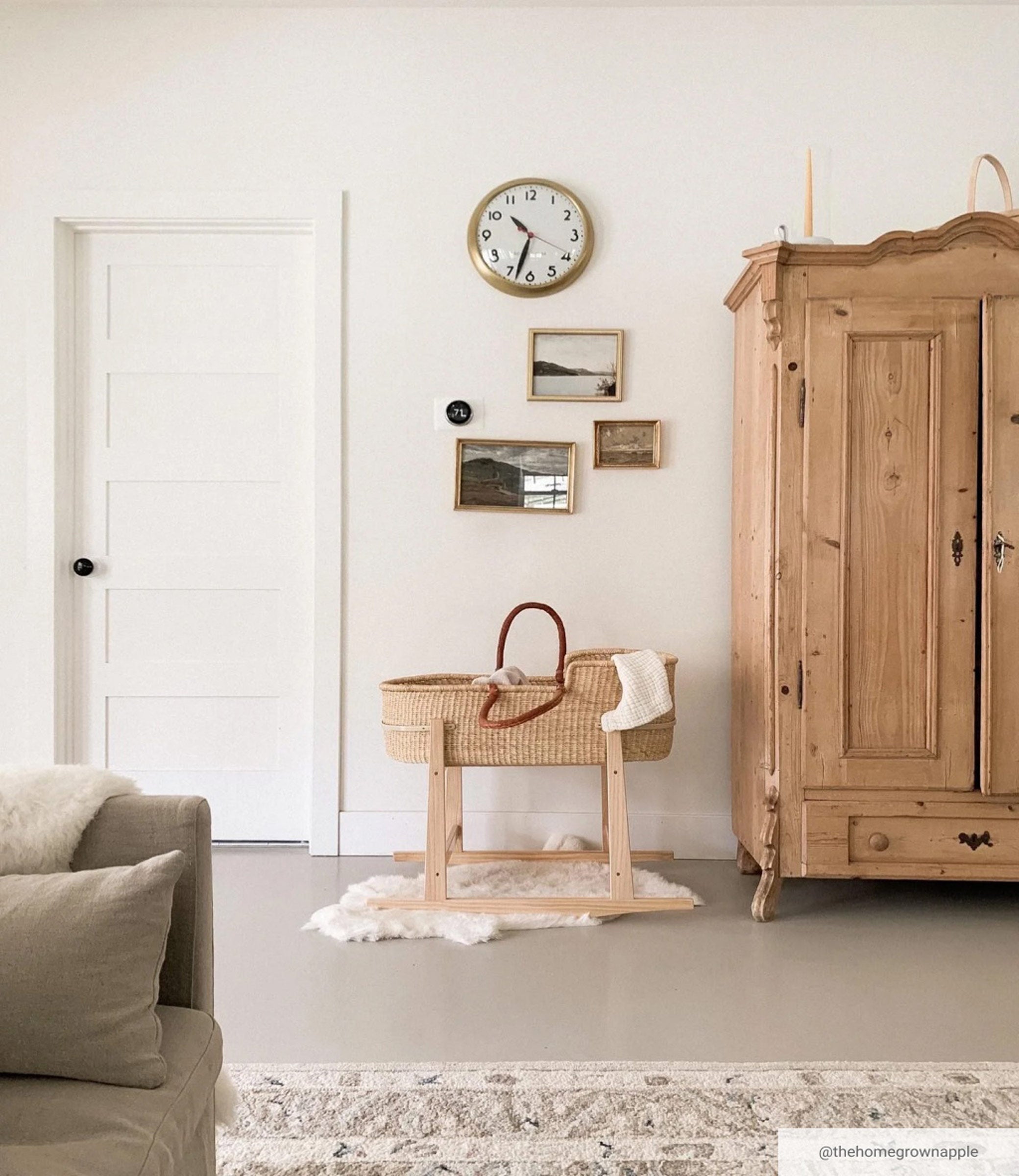 Brass wall clock above baby bassinet in living space next to oak wardrobe.