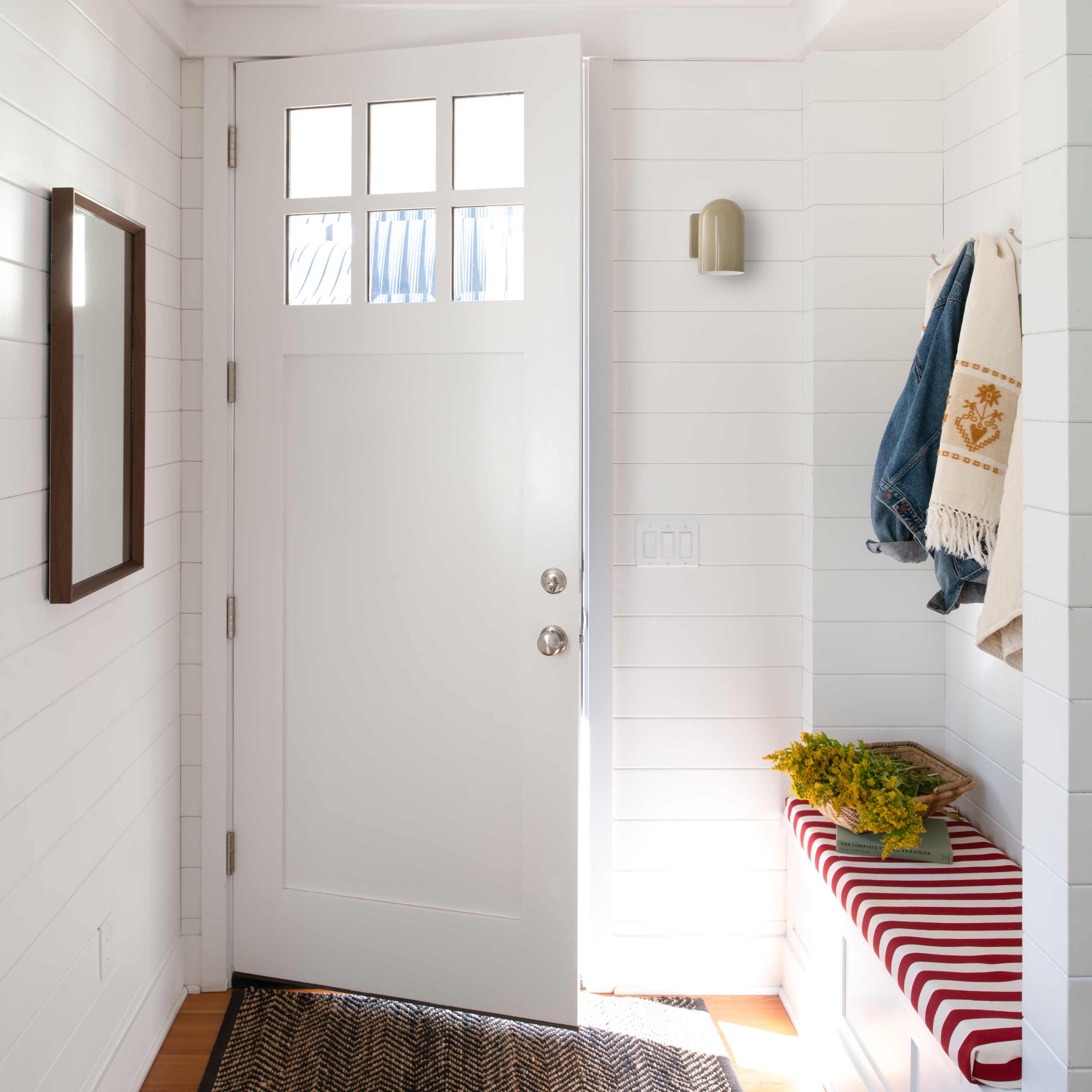 Light and bright entryway with bench nook and hooks and mirror on opposite wall.