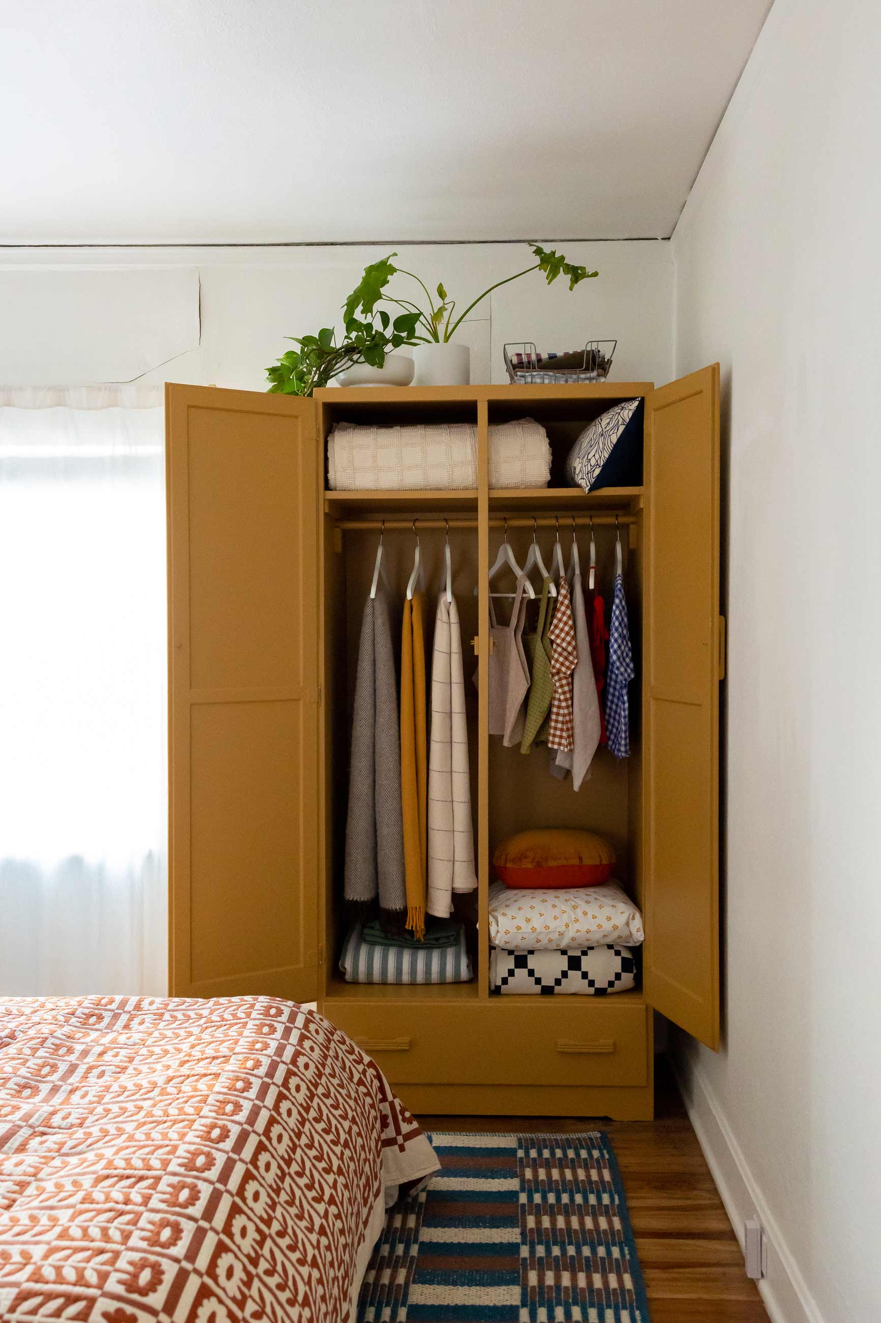 Yellow armoire with doors wide open showing blankets and handmade clothing inside.