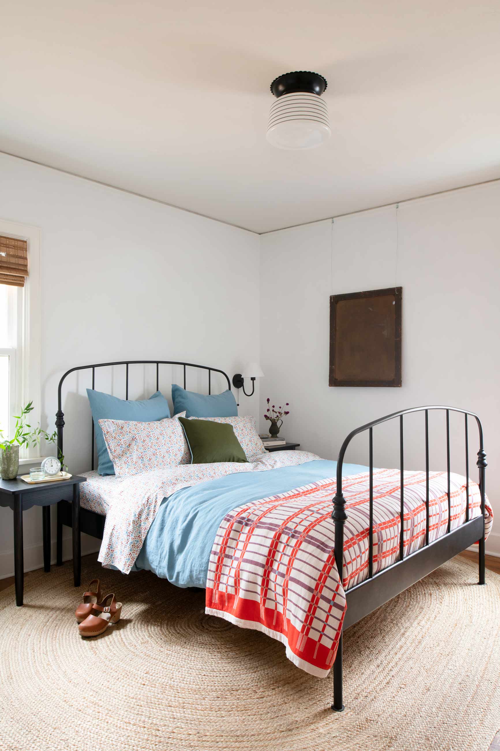 Bright blue and red bedding on black bed frame in sunny bedroom. 