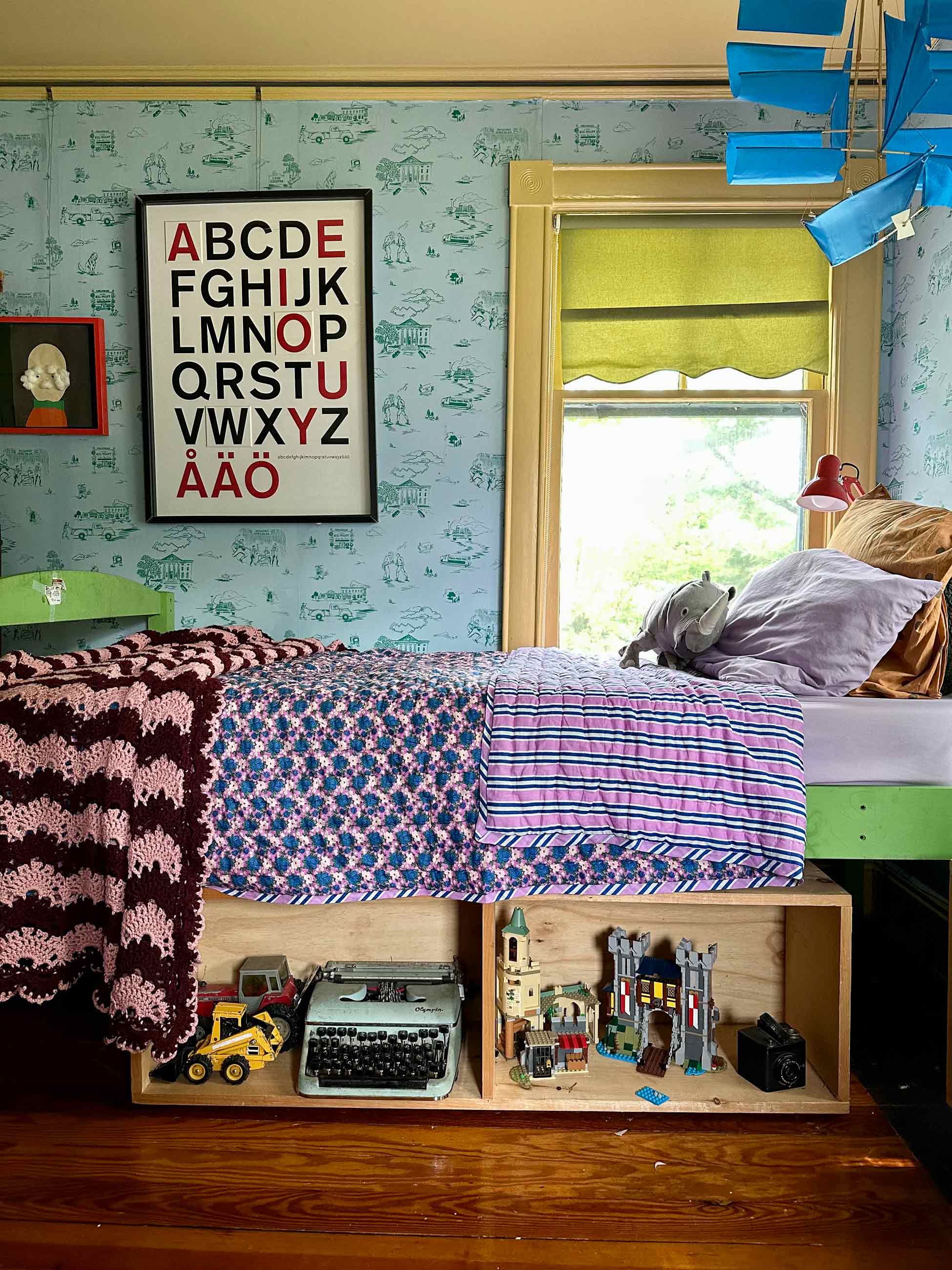 Brightly colored kids room with alphabet print on wall above bed.