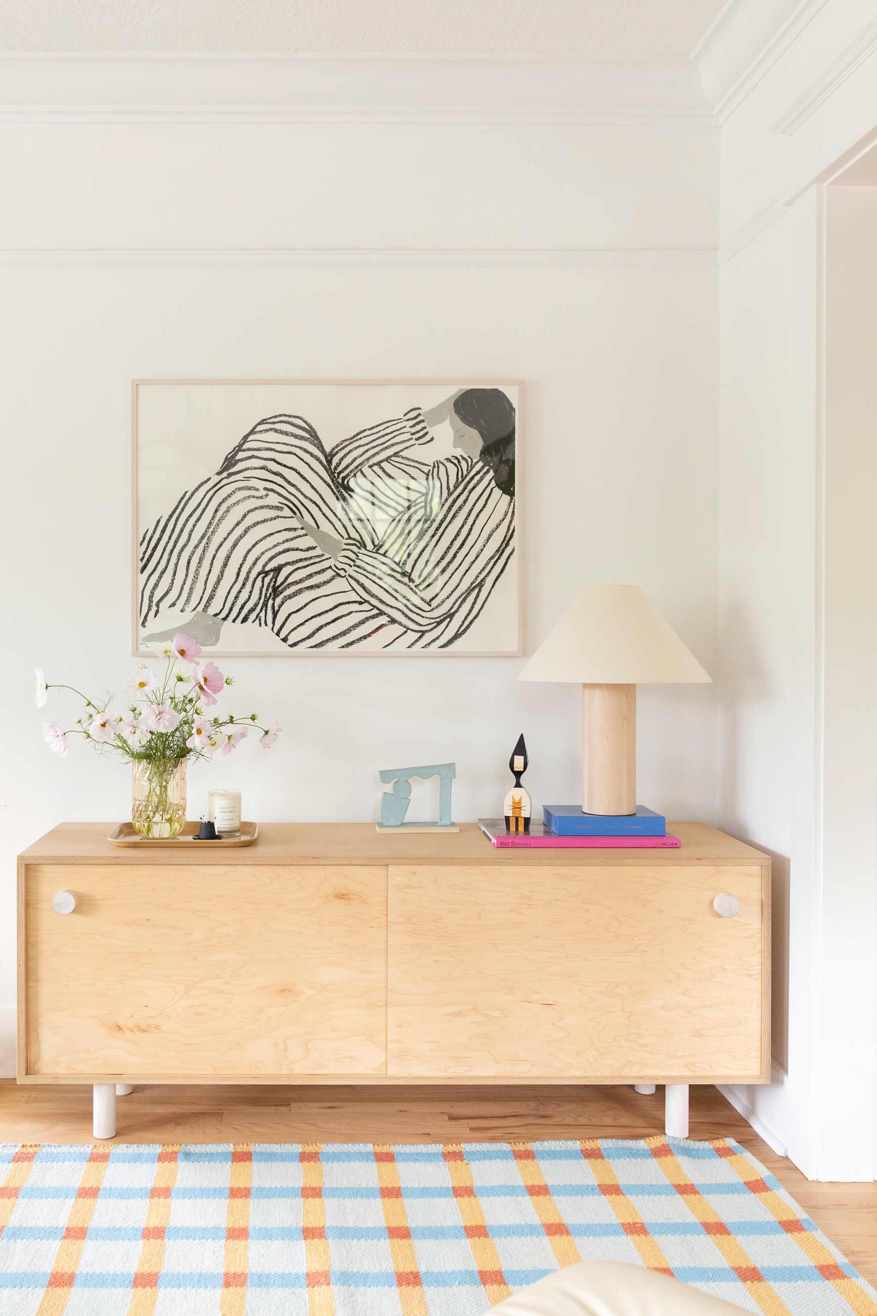 Light wood buffet with plaid wool rug and wooden lamp.