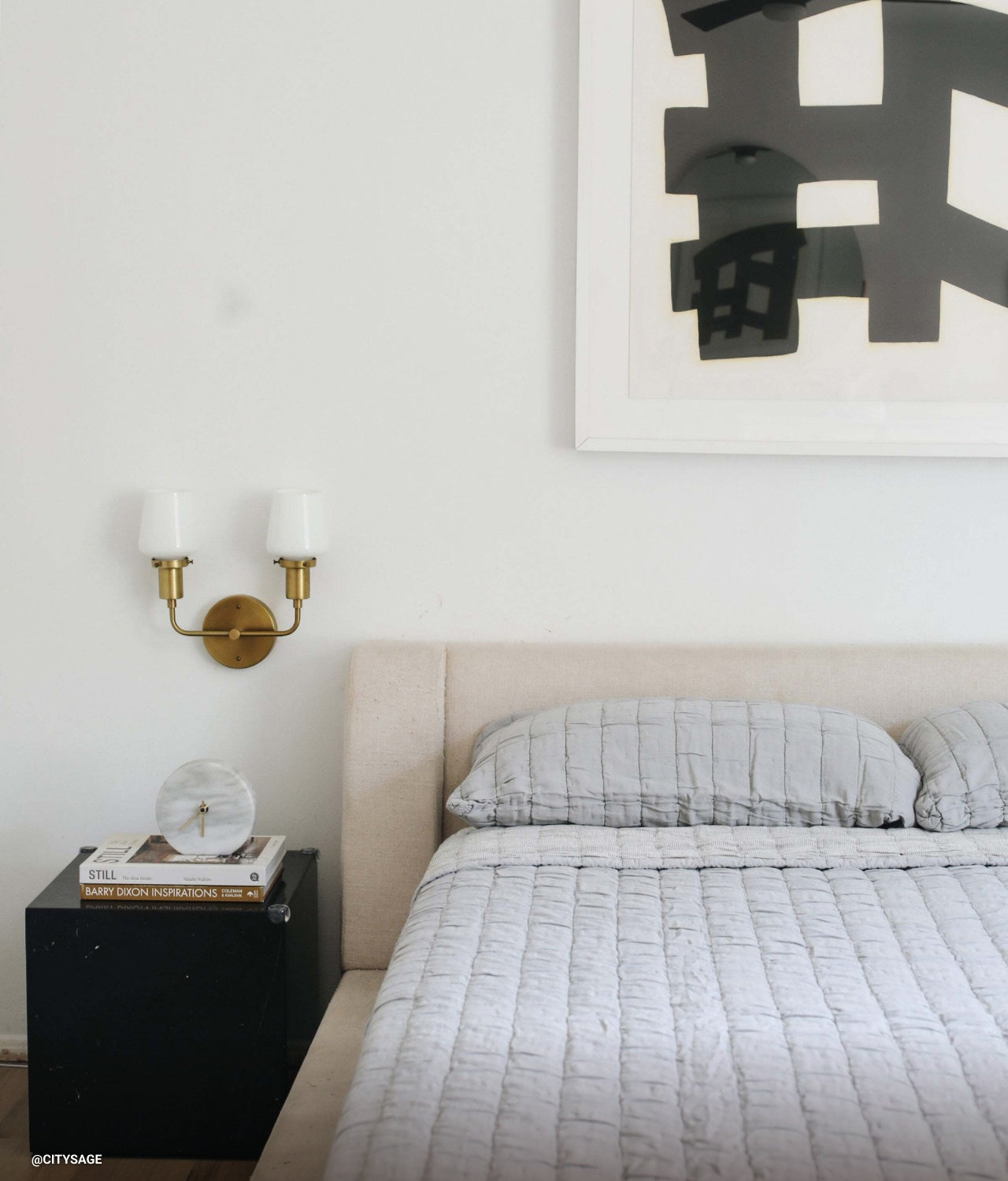 A neutral bedroom with a wall sconce via @citysage.