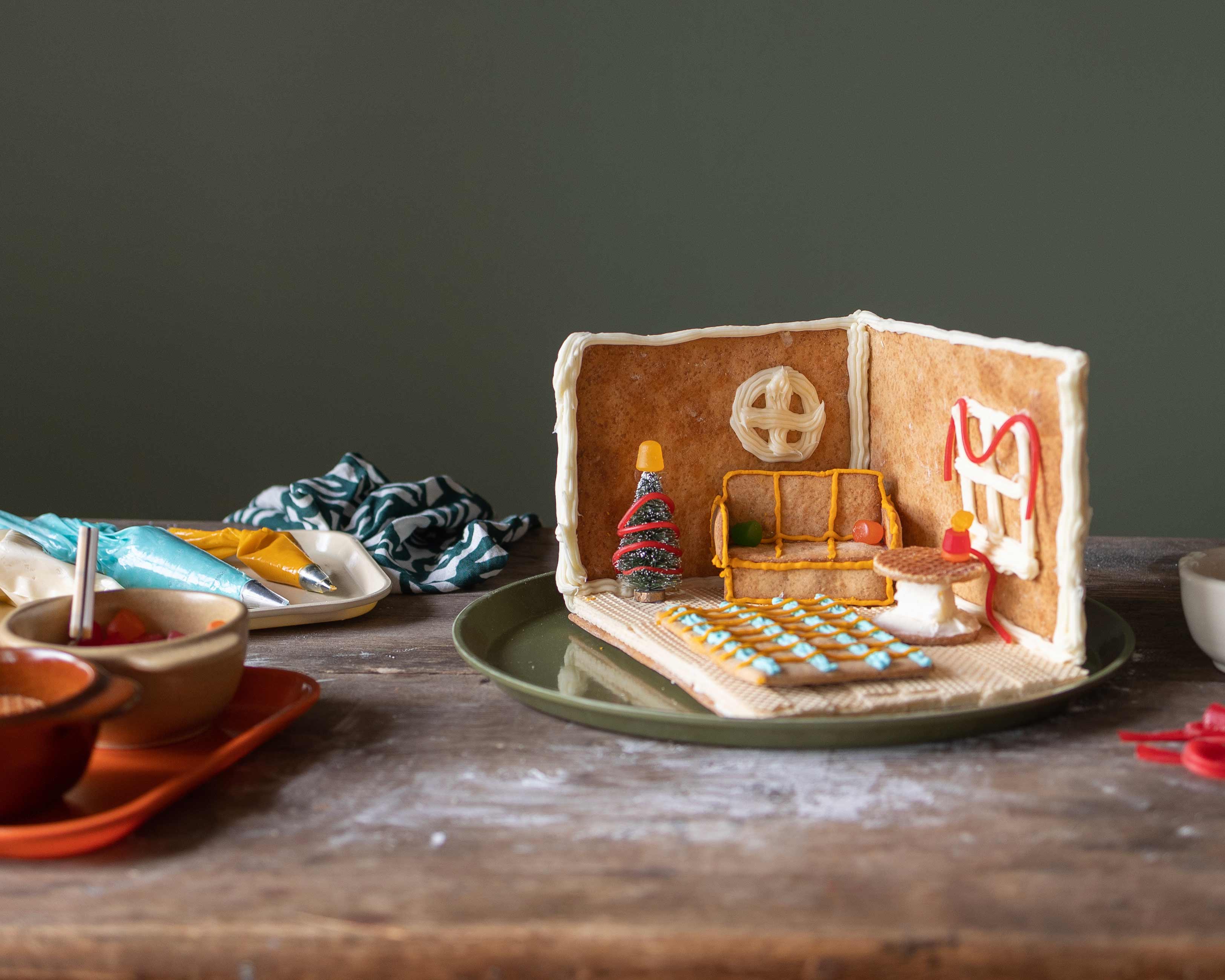 Closeup of gingerbread room on wood table with trays full of decorations and candy.