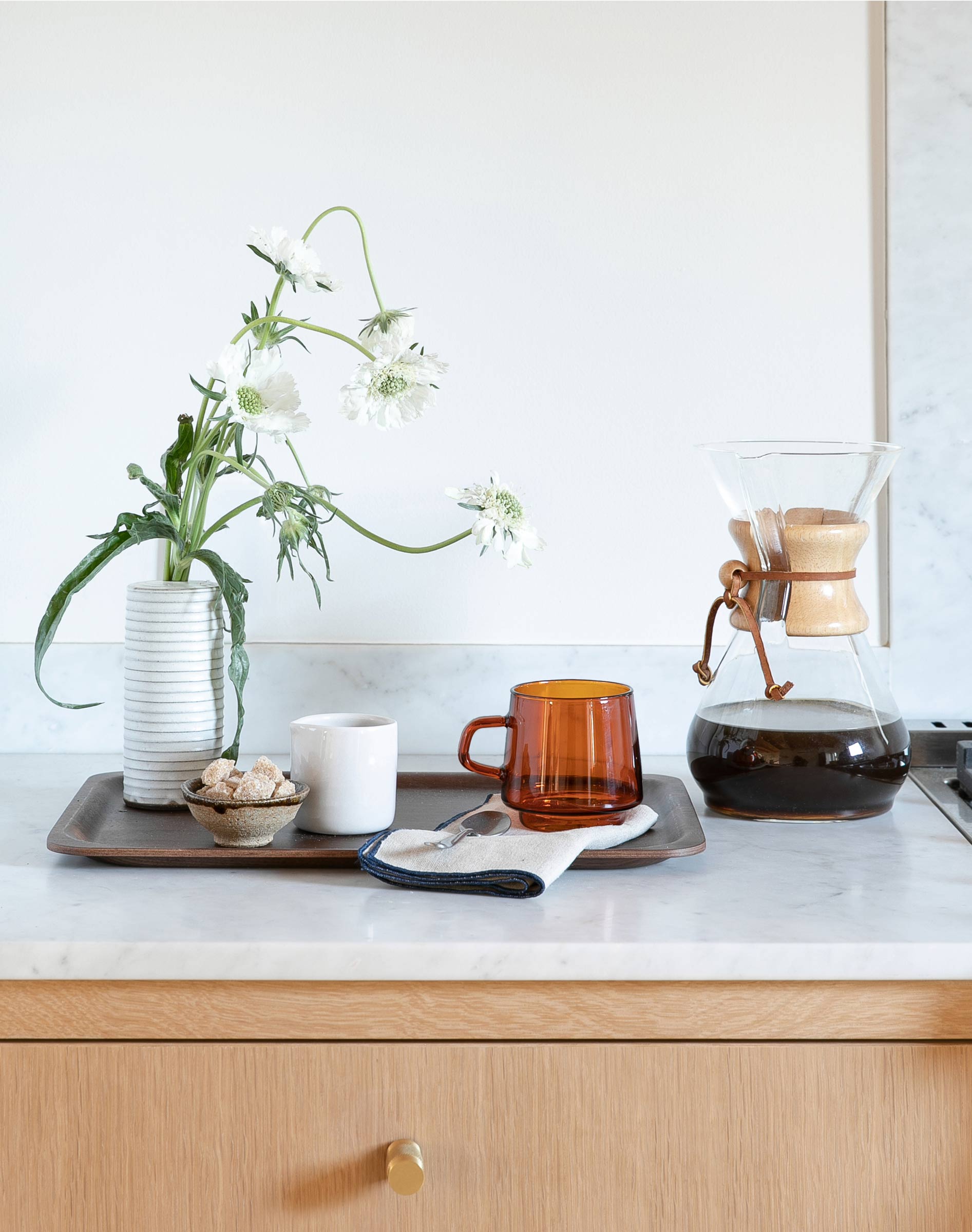 A cup of coffee with a chemex on the kitchen counter. 