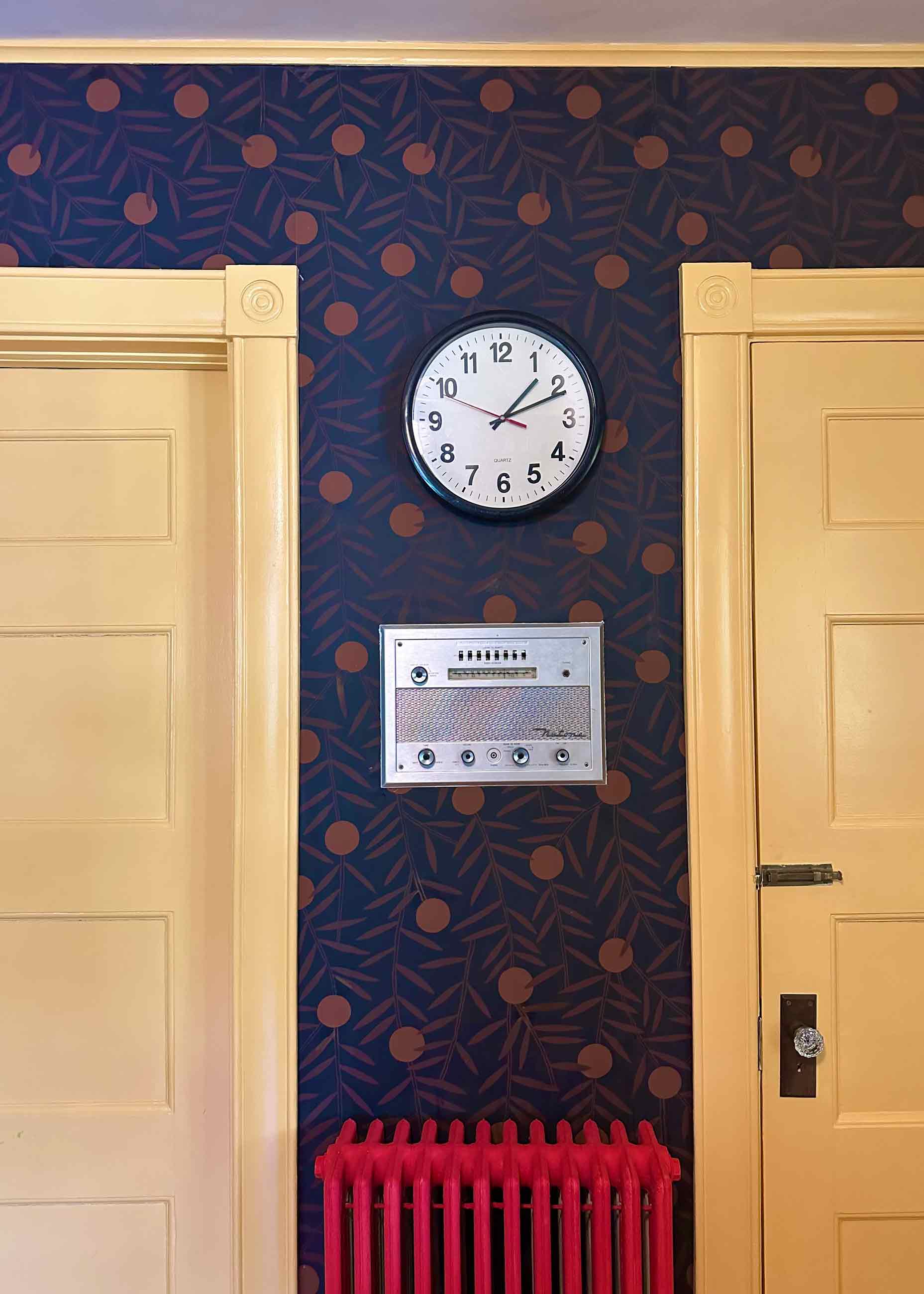 Kitchen wall with red radiator and black clock.