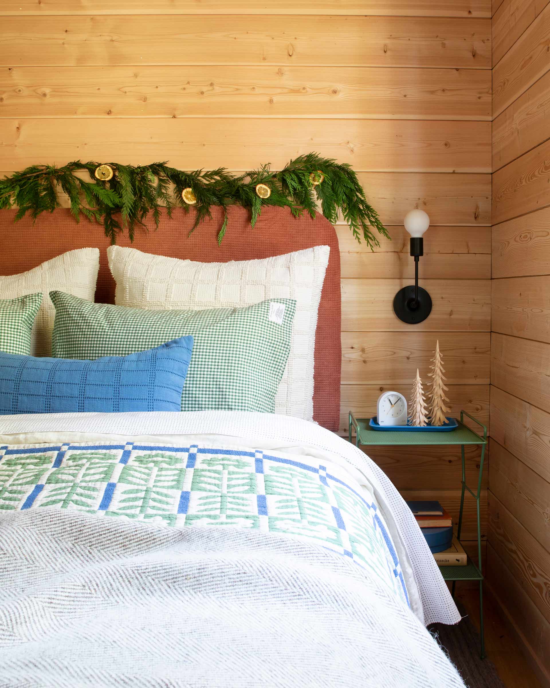 Cozy cabin bed with floral quilt and garland on headboard.