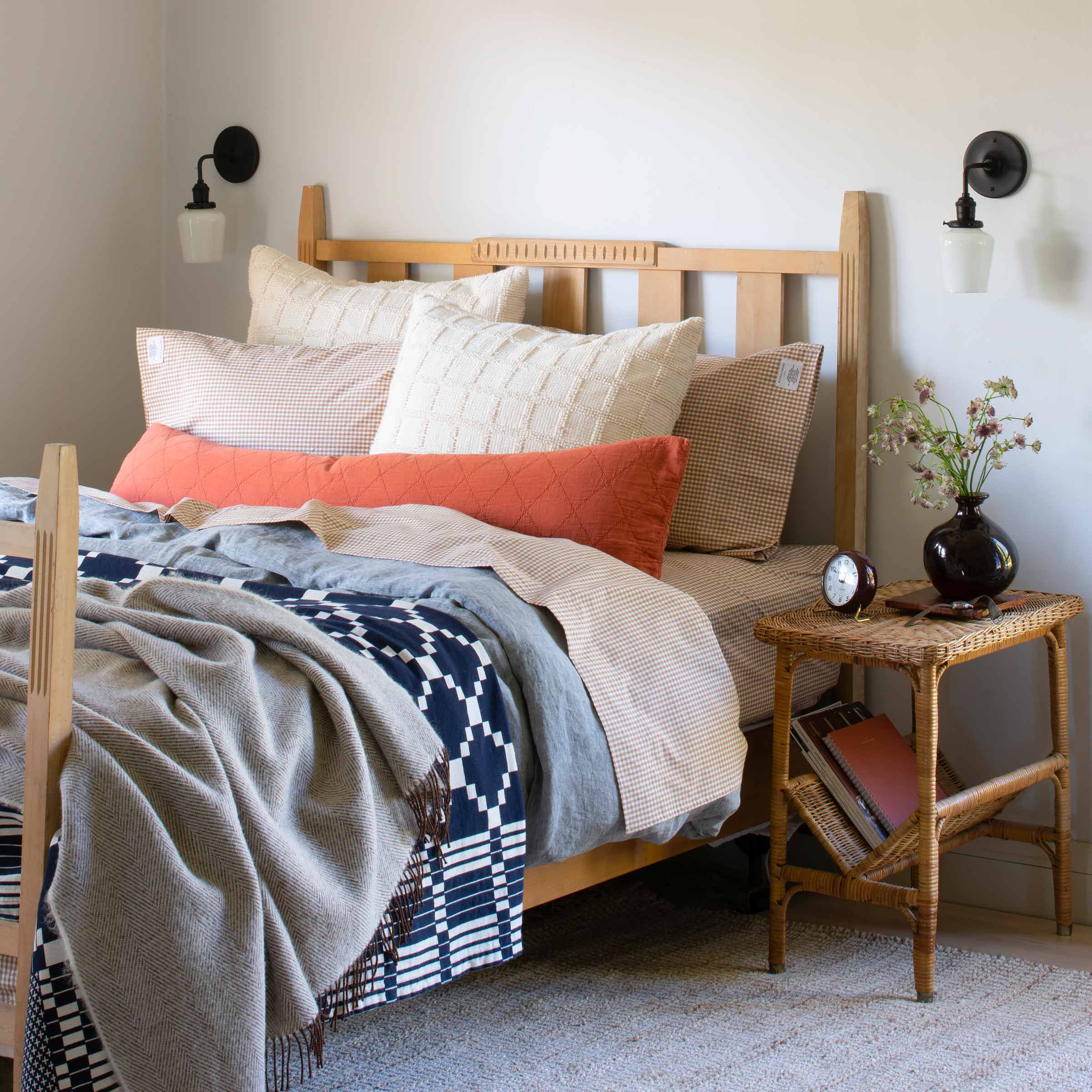 Cozy bed with heirloom quilts, bedside reading sconces, and a wicker side table. 