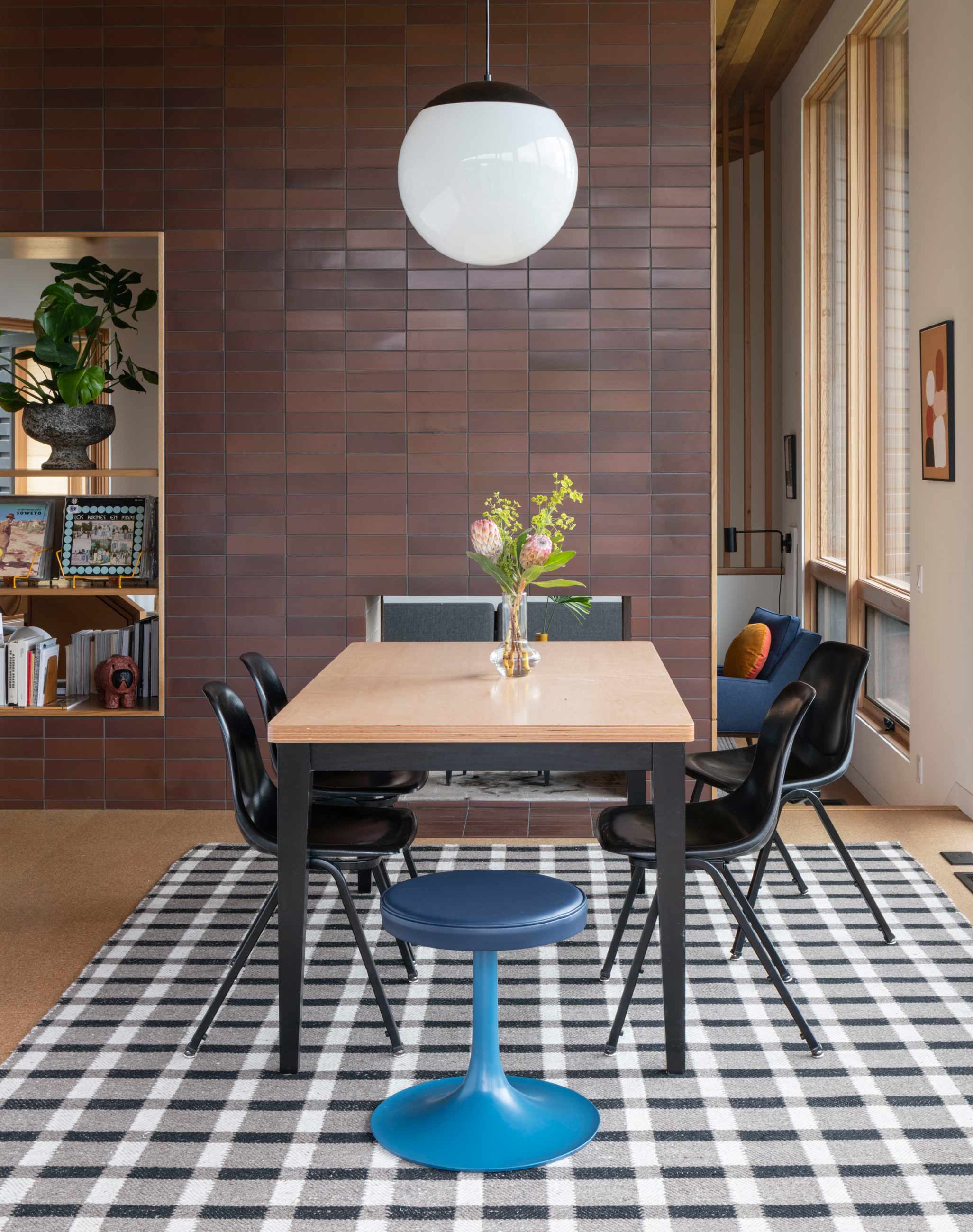 Modern dining room with wooden table, classroom chairs, and blue stool.