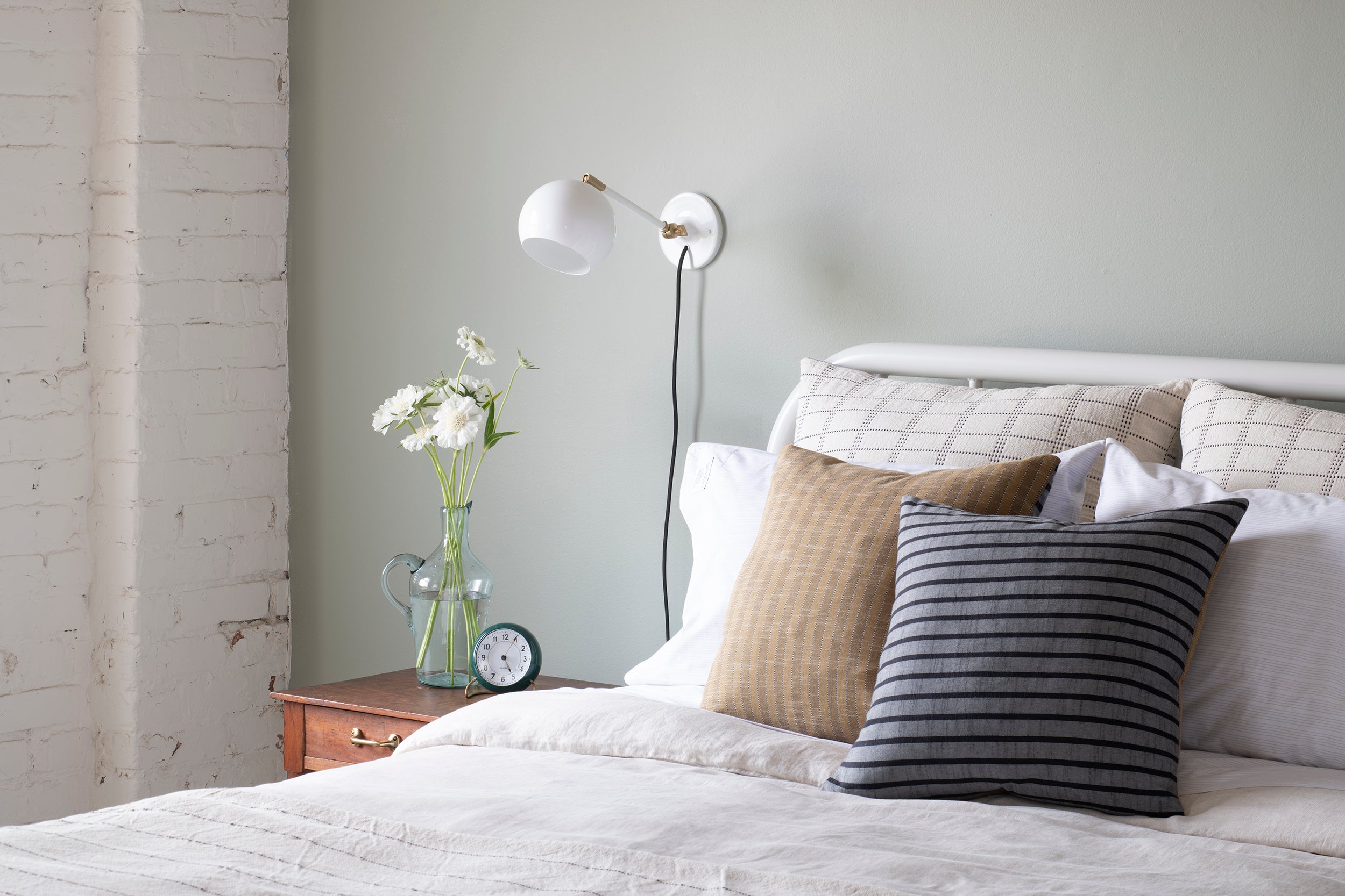 bed with a white bed spread and a white wall with white flowers and a white light fixture