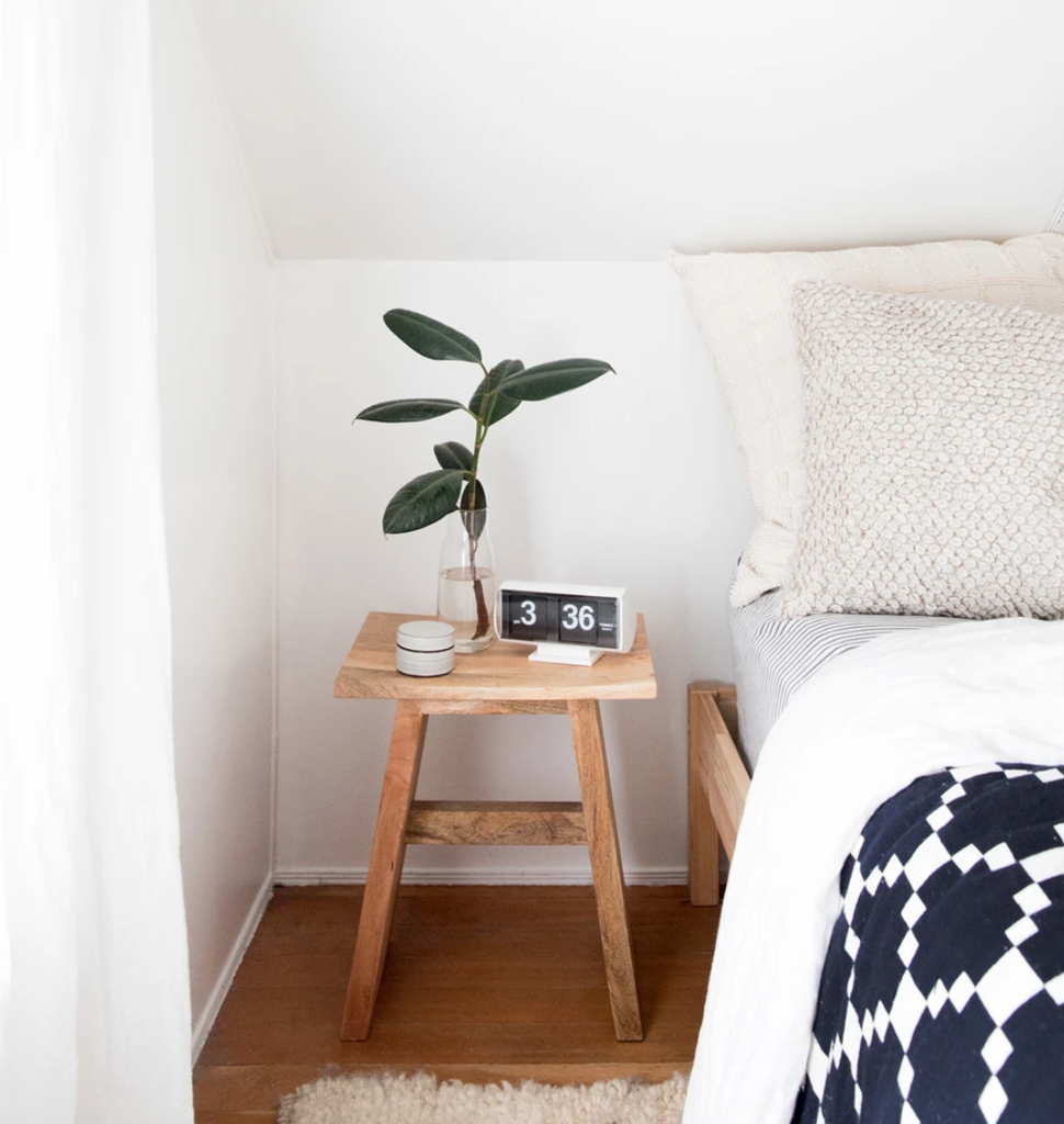 small wooden table with a plant on it next to a bed