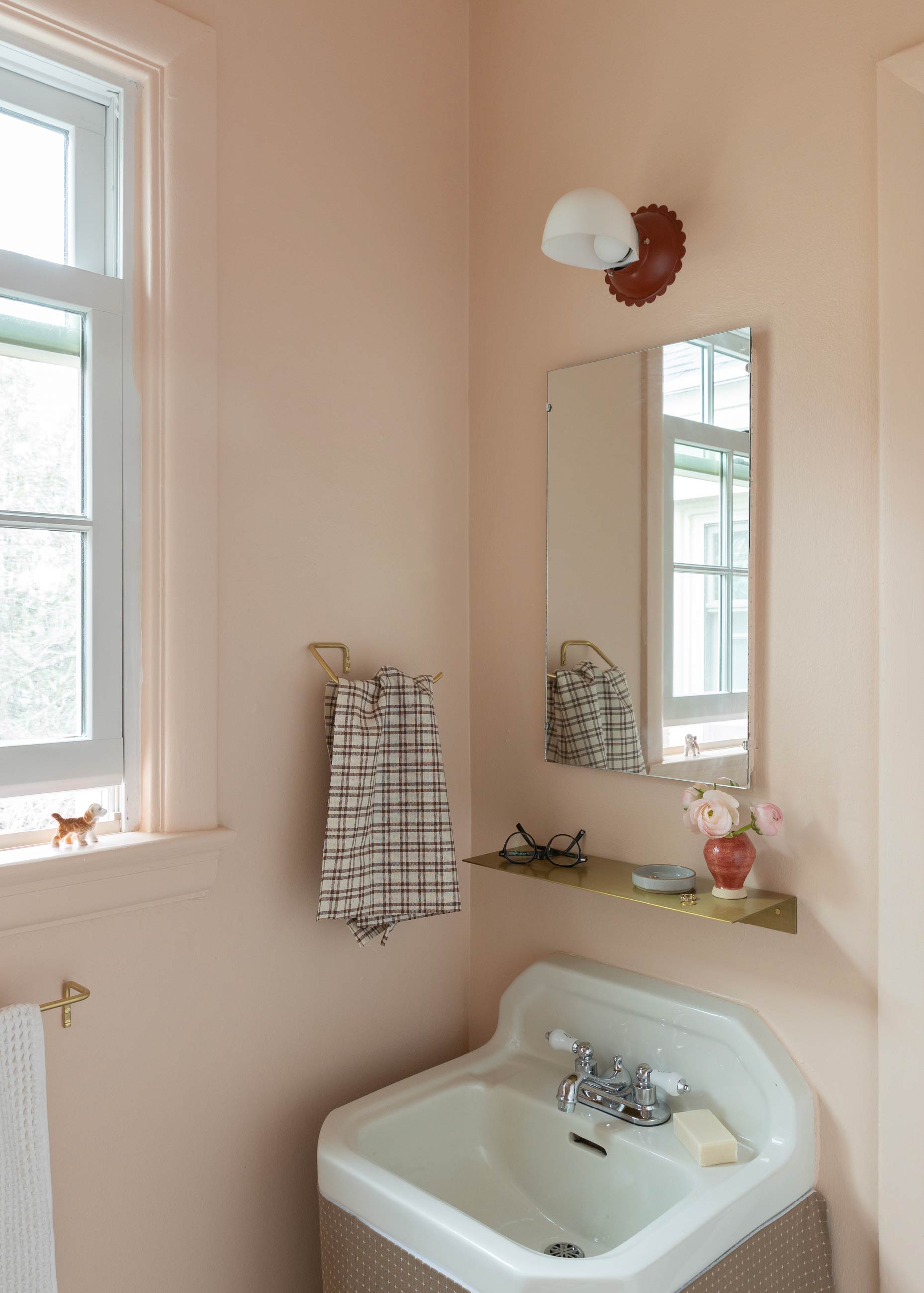 Pink bathroom with scalloped light fixture above sink.