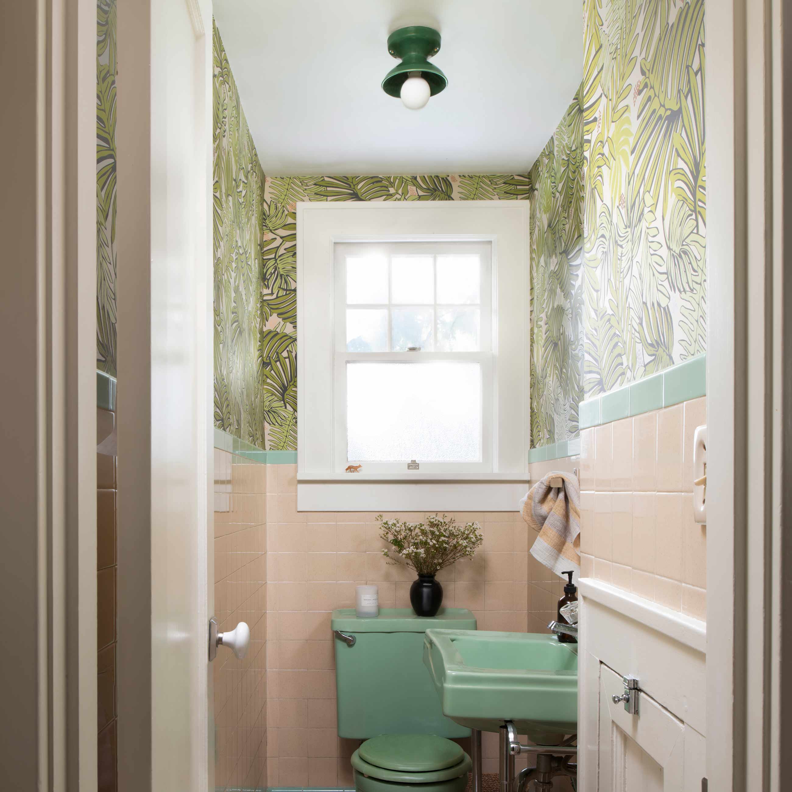 Pink and green powder room with dark green light fixture. 