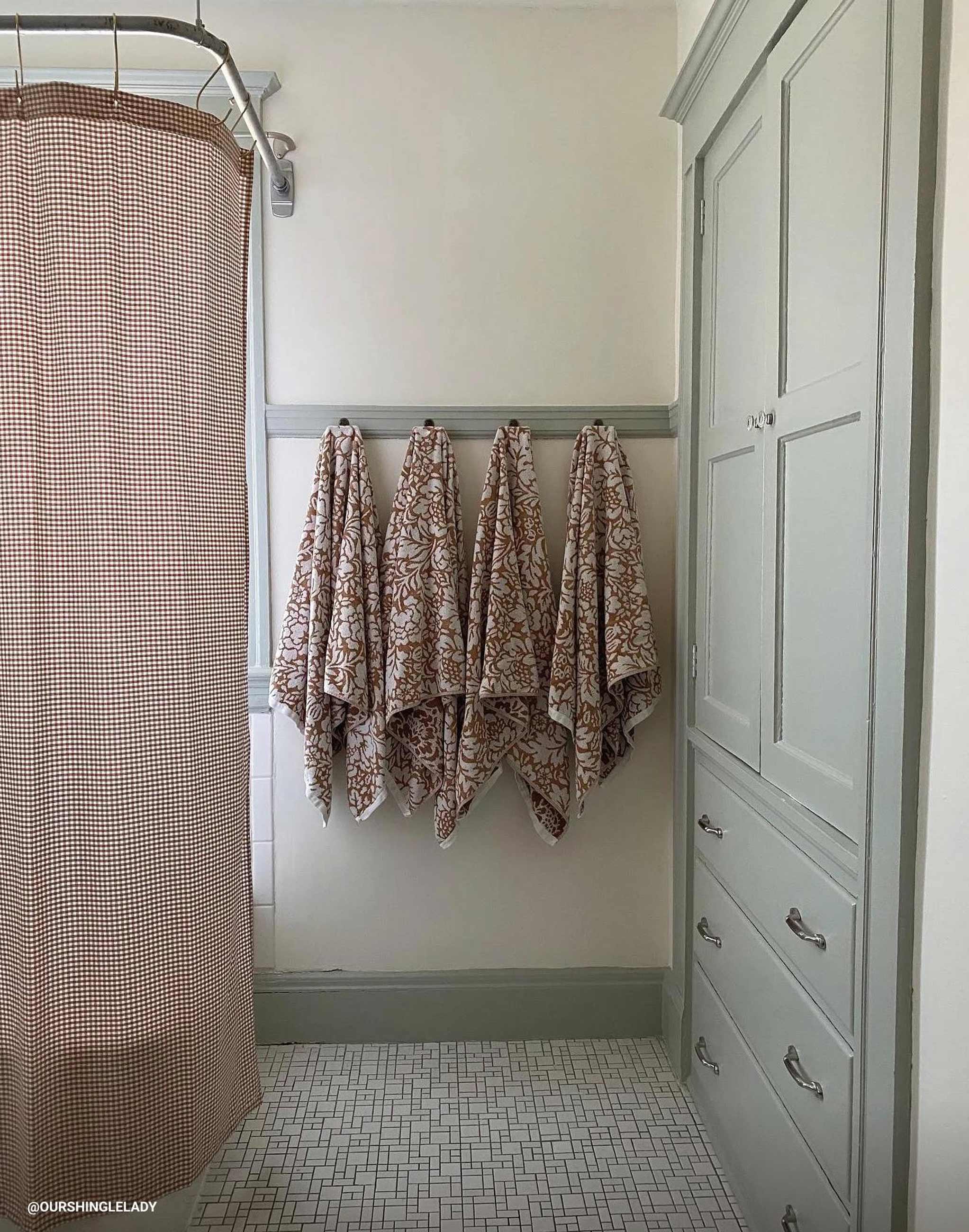 Green bathroom with gingham shower curtain and hanging towels. 