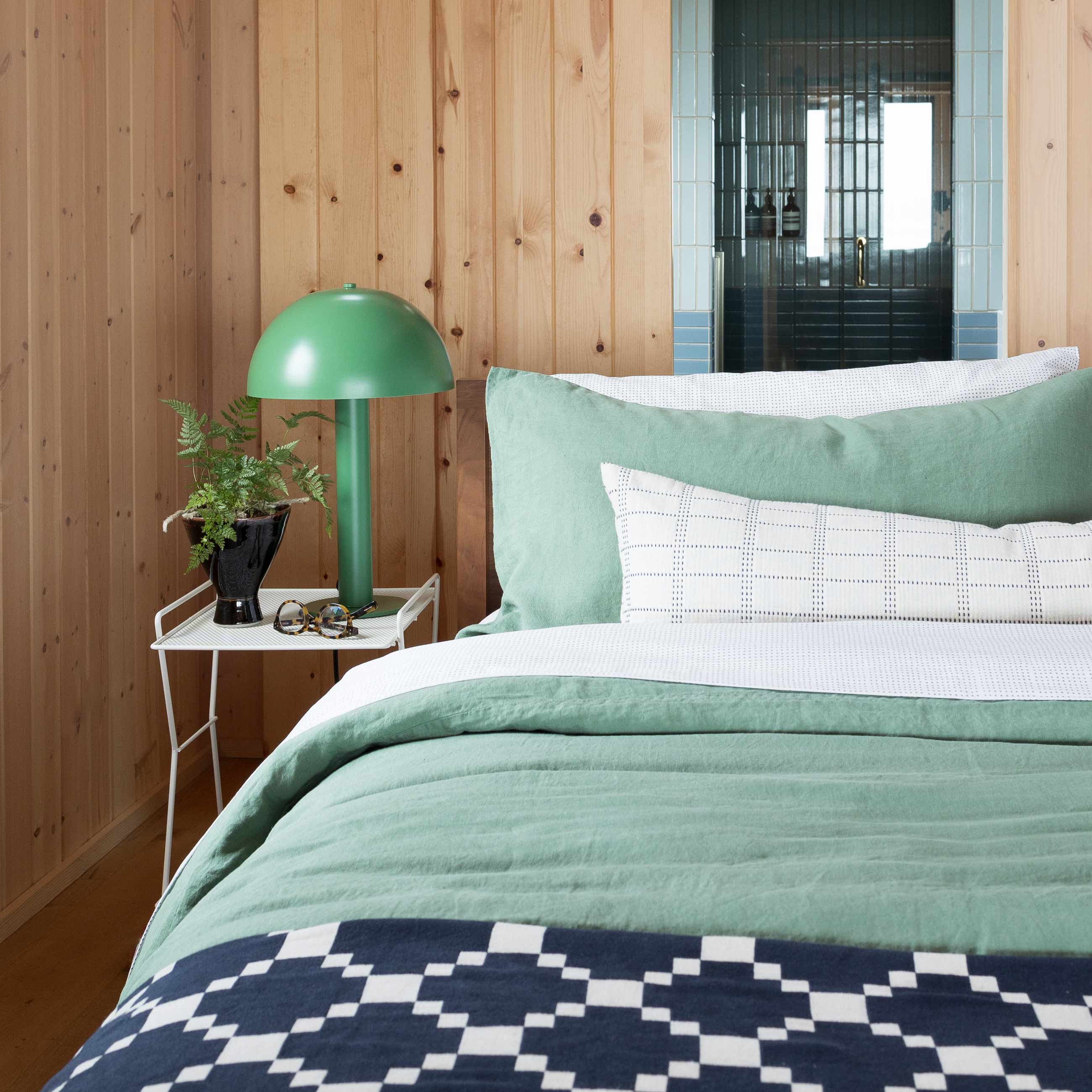 Cozy green bed with white bedside table holding green lamp. 