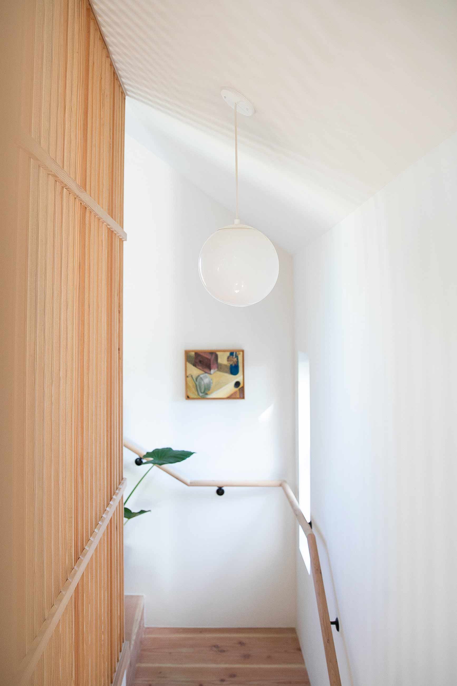 Bright hallway staircase with large white globe pendant. 