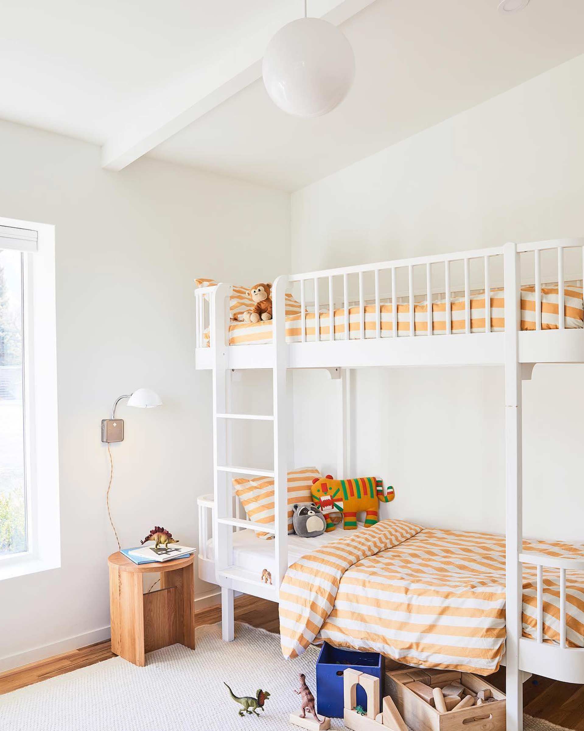 A kid's bunk bed with striped bedding and a wall sconce for reading. 