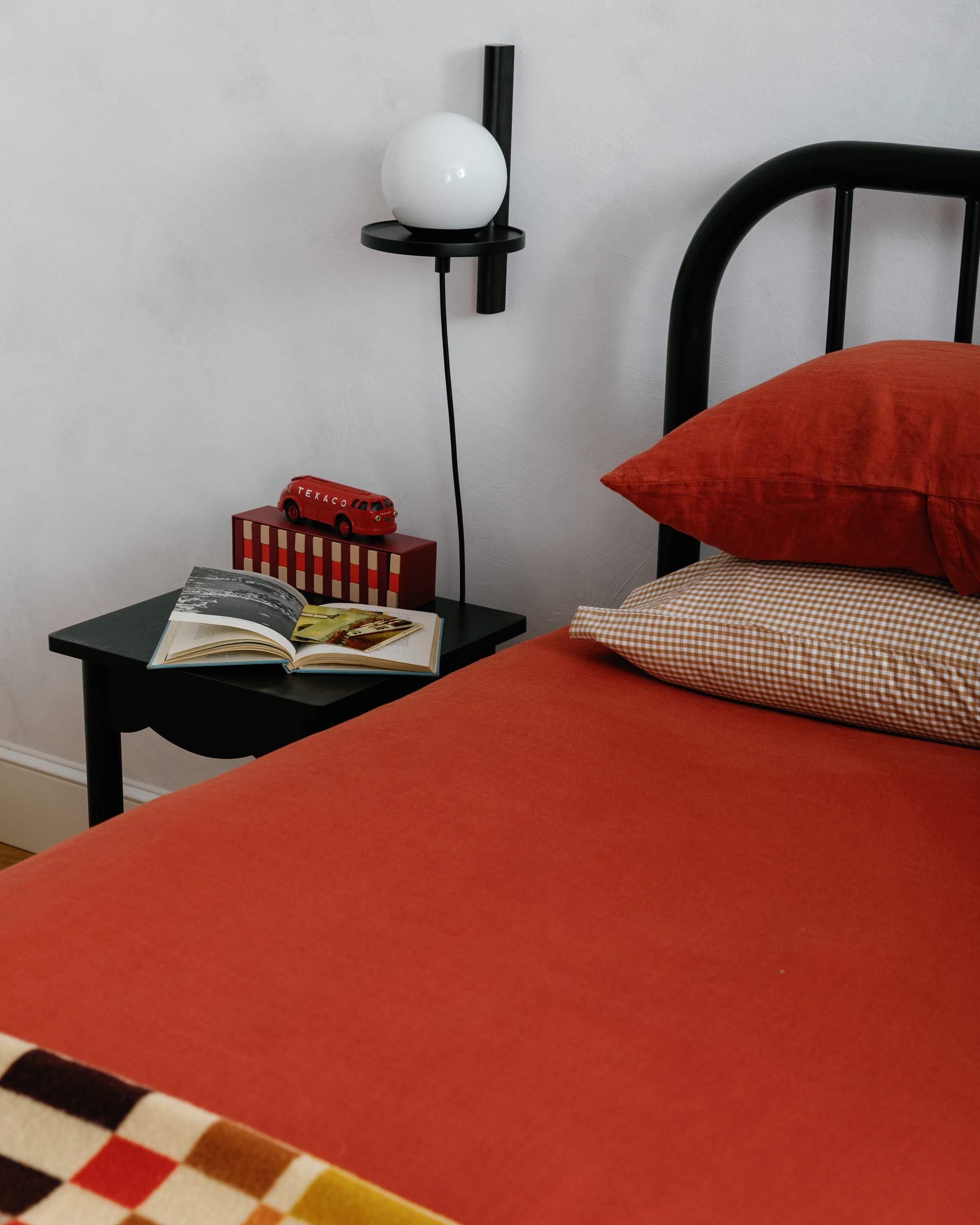 Red bedding with a black side table and wall sconce.