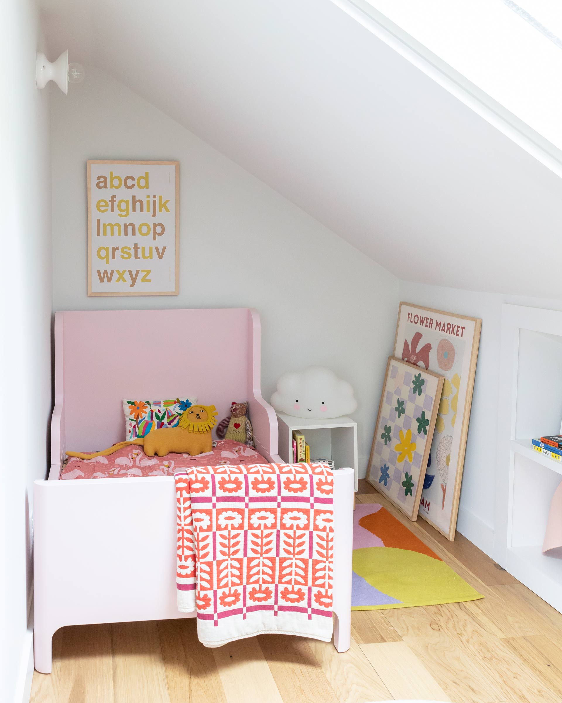 Kid's room with a vaulted ceiling, colorful floral bedding, and art prints. 