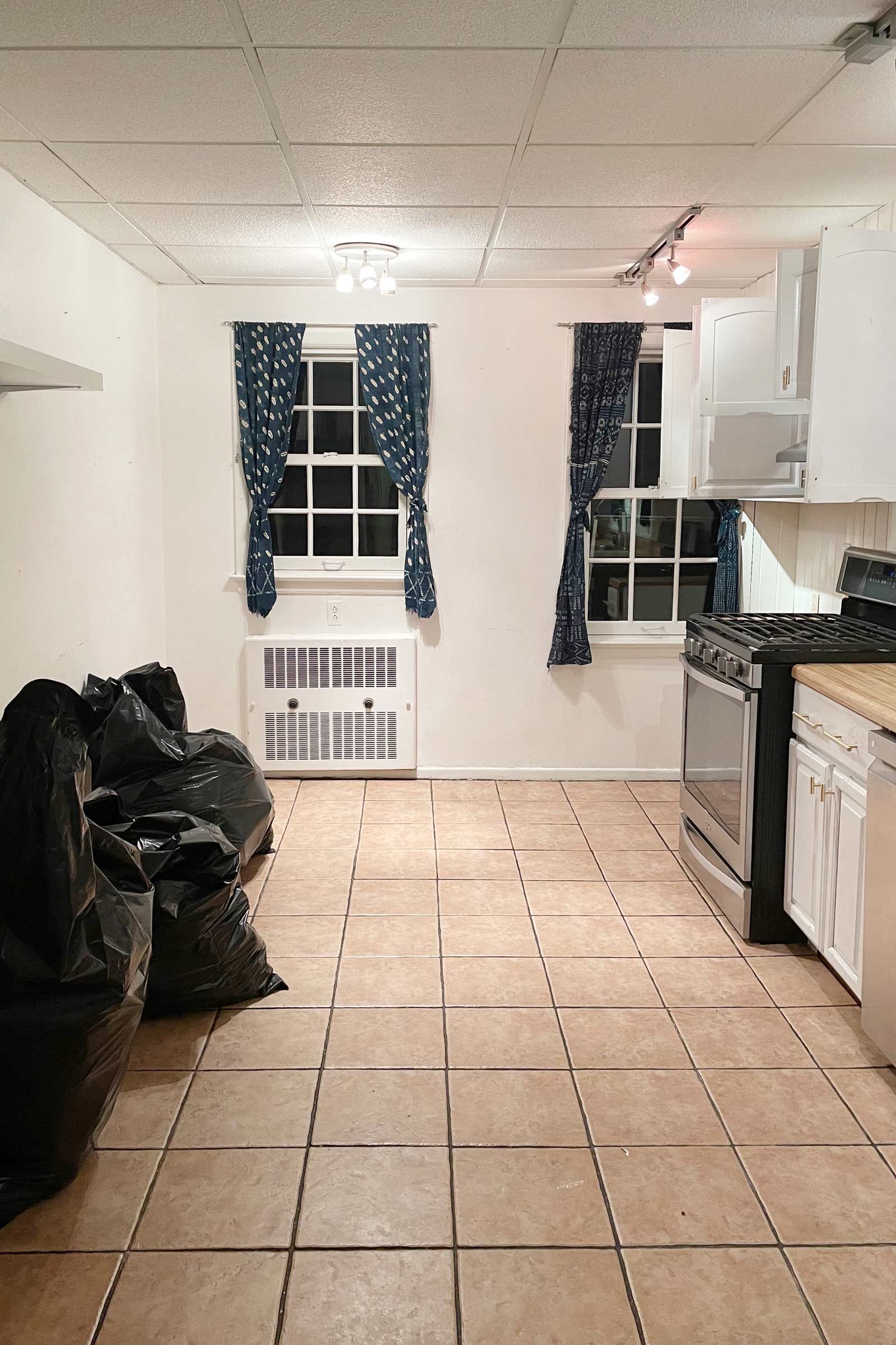 Kitchen before renovation with windows, drab curtains, and outdated lighting.