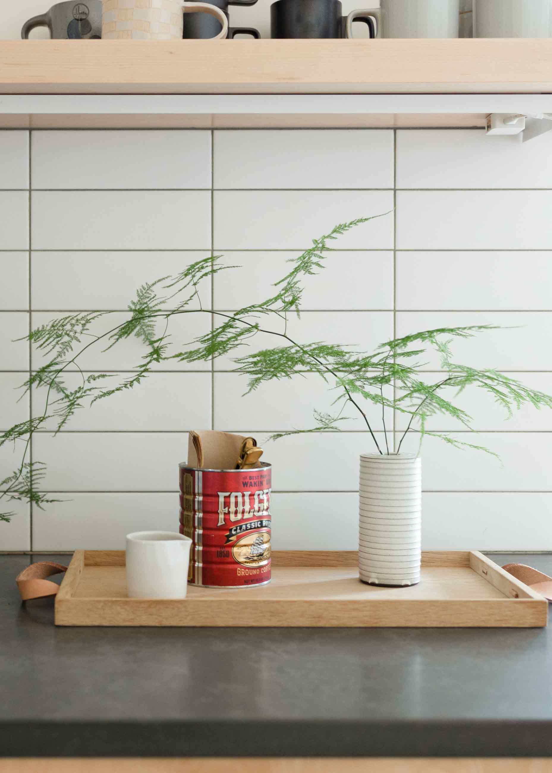 Kitchen shelf and counter with mugs and coffee tin.