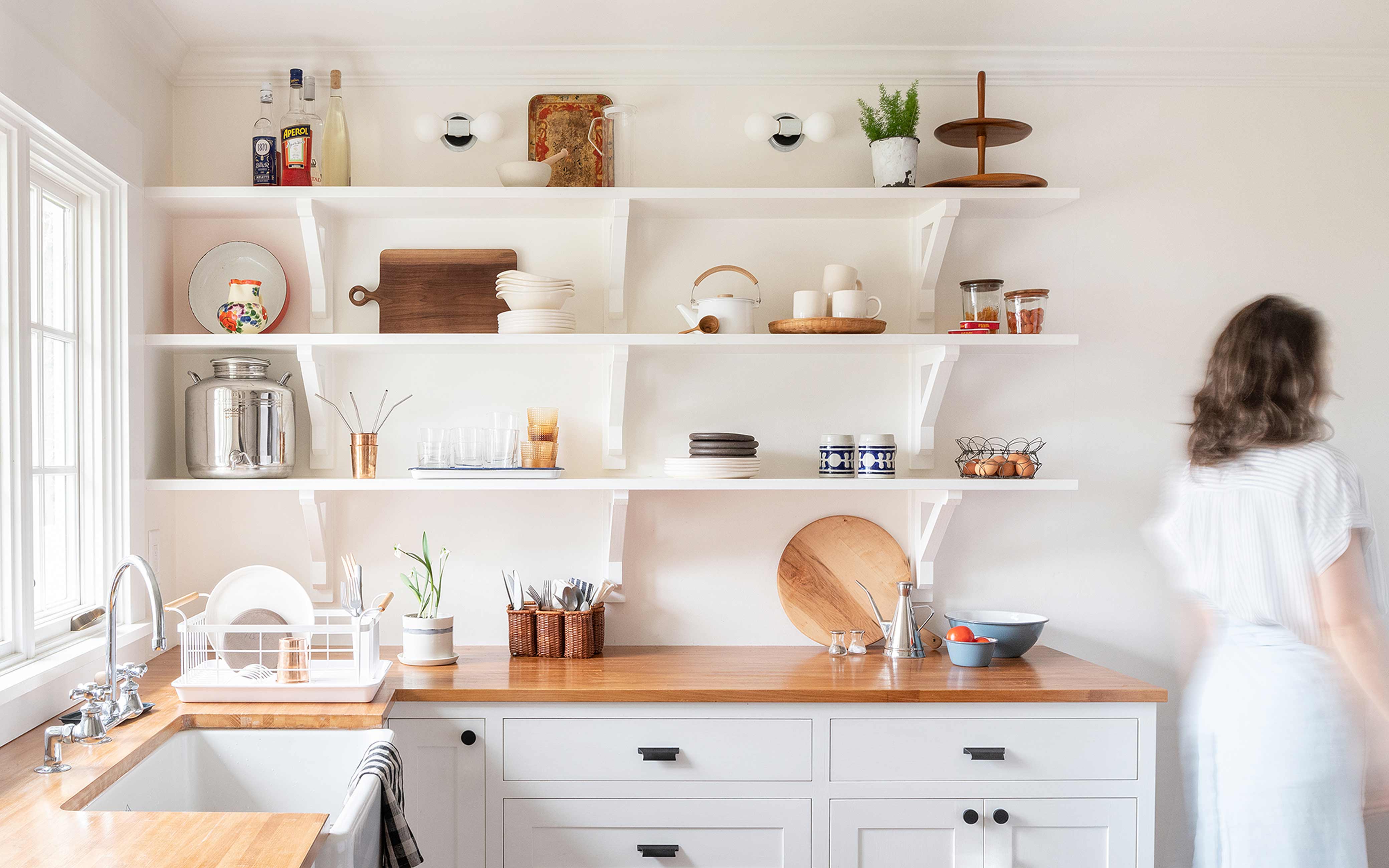 Open shelving in kitchen with person walking by.