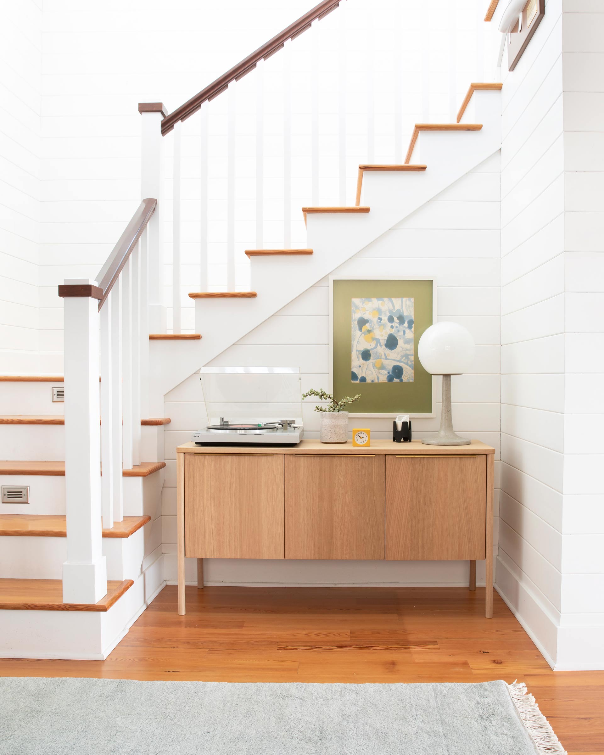 Matter table lamp on natural wood credenza at the bottom of a staircase.