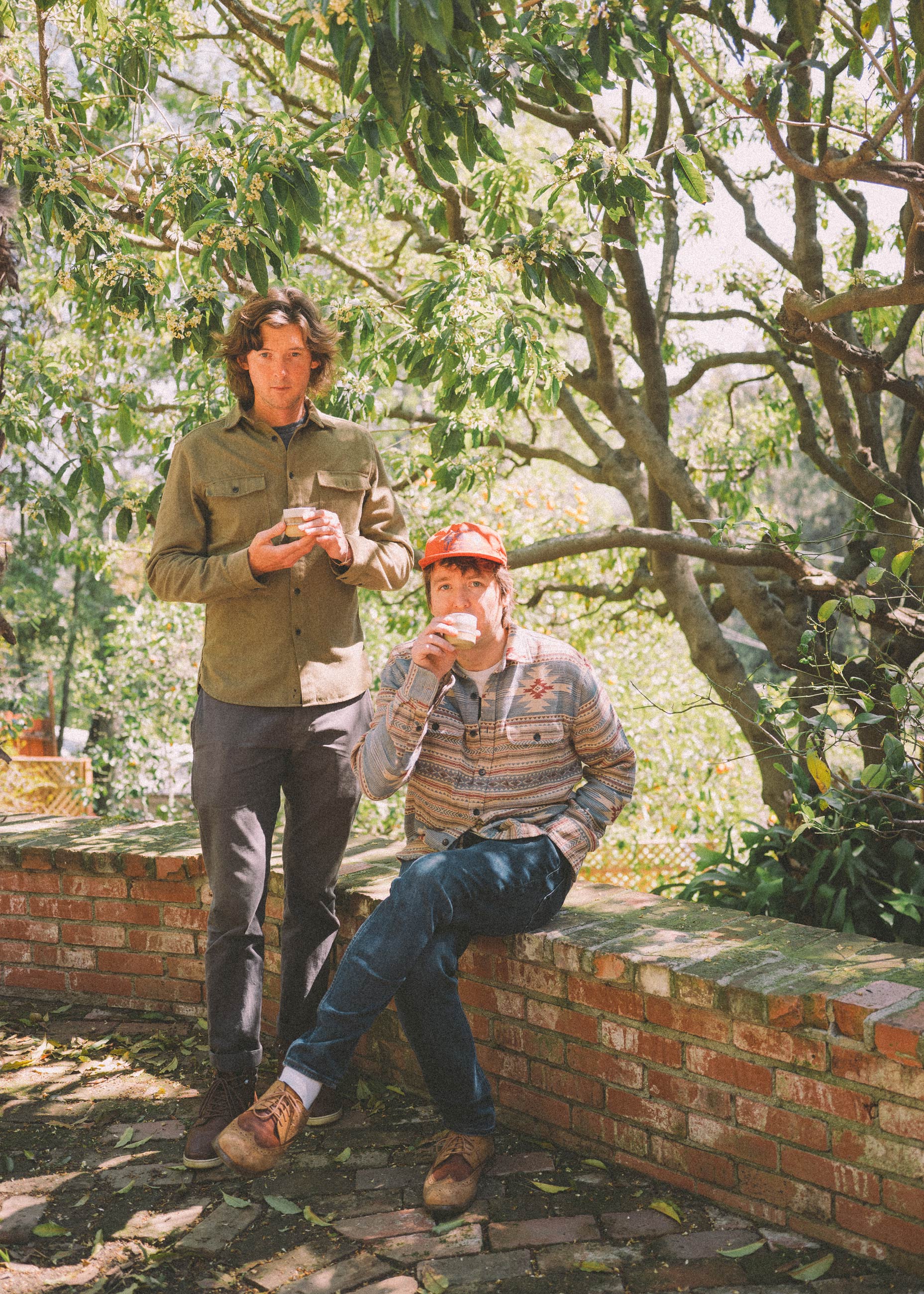 The band, Milk Carton Kids, standing outside in a garden drinking coffee.